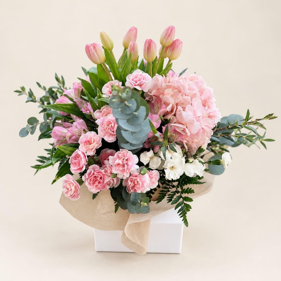 Pink tulips and carnations arranged with pale pink hydrangea in a wrapped box