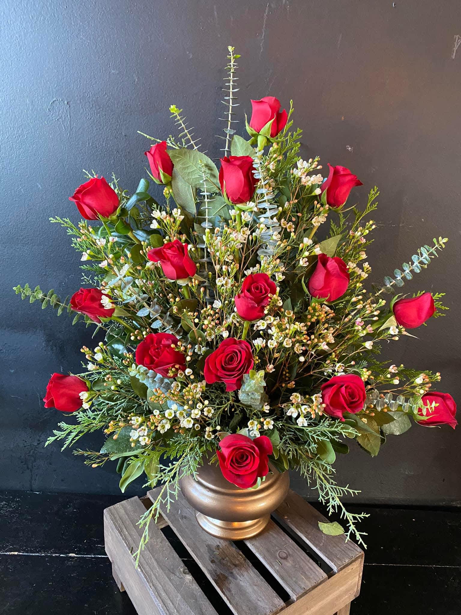 Red roses arranged in a gold vase with mixed greenery