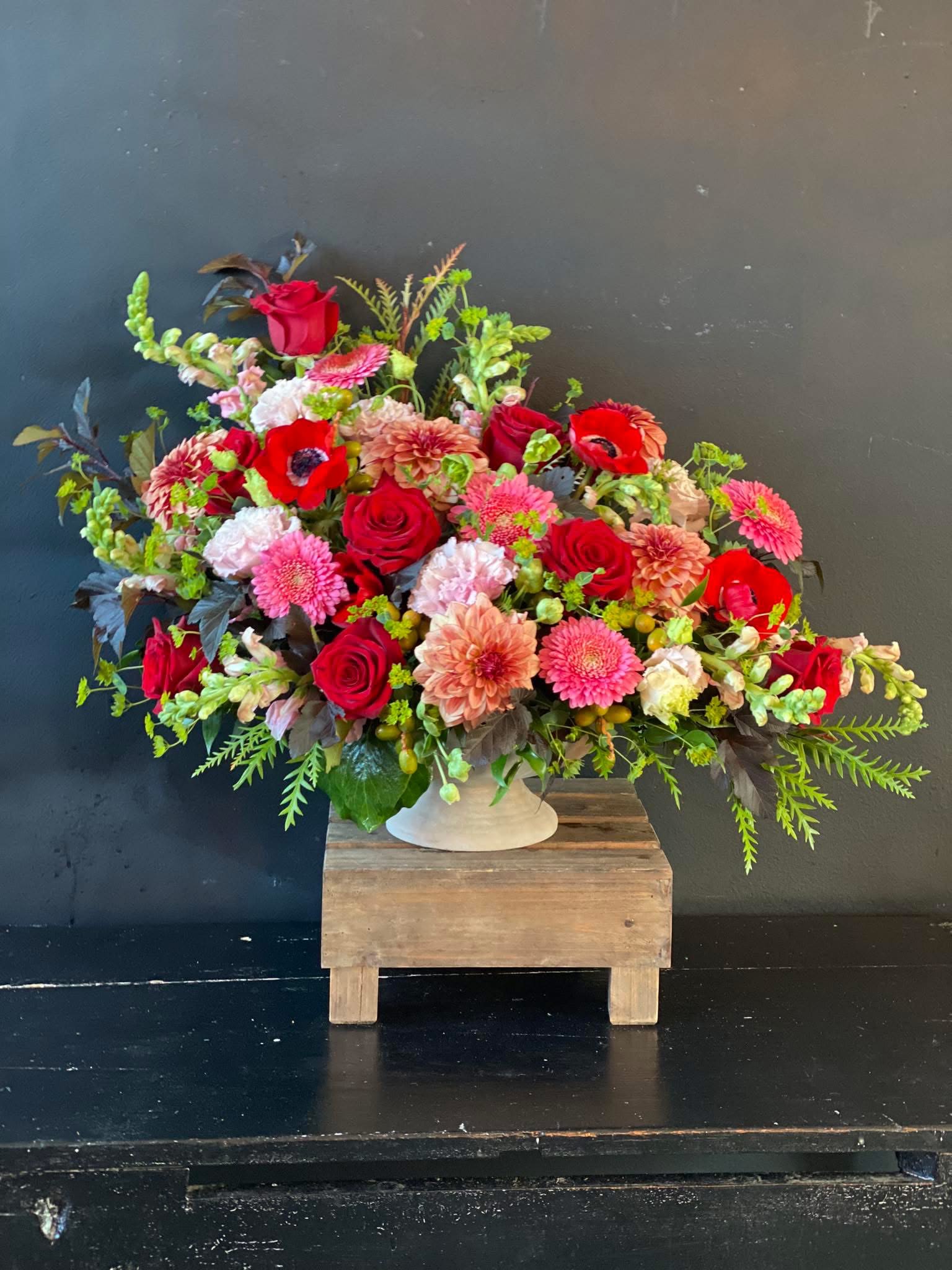 Large mixed bouquet of red, pink, and peach flowers in a white vase