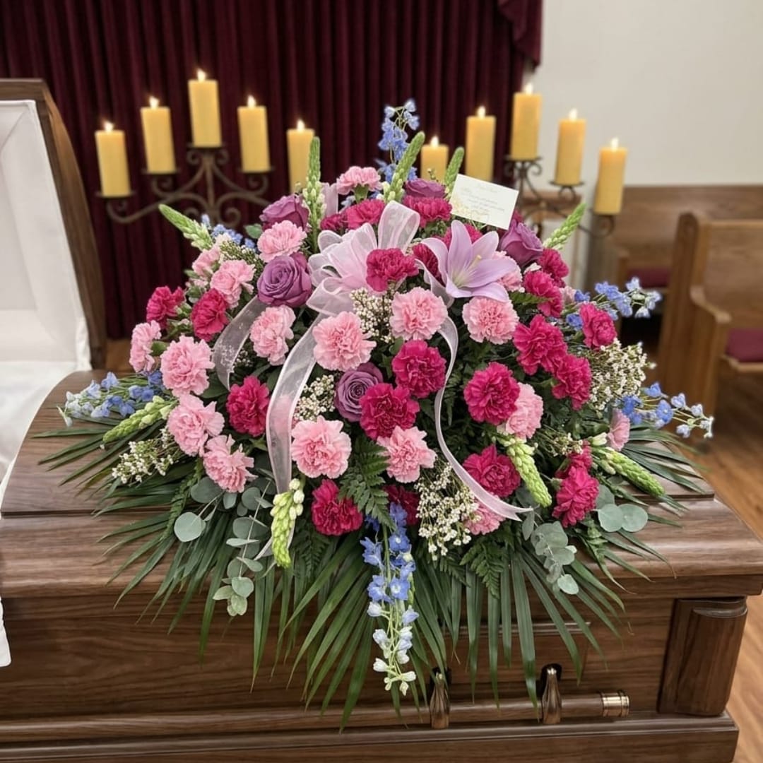 Pink and purple funeral spray on a casket with candles in the background