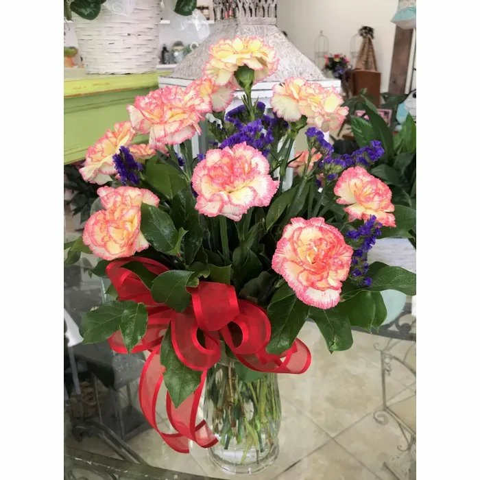 Bouquet of pink and yellow carnations with purple filler in a clear vase