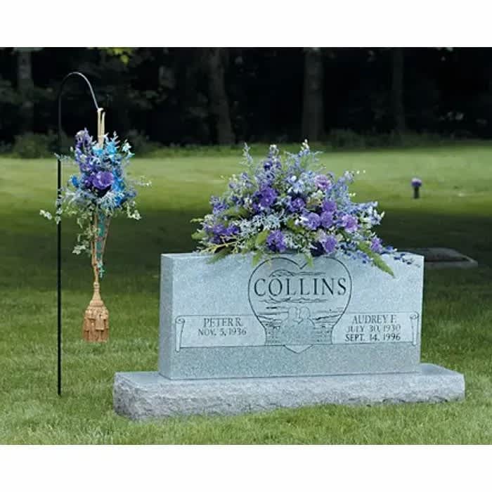 Purple and blue floral arrangement on a gravestone with a hanging floral piece nearby
