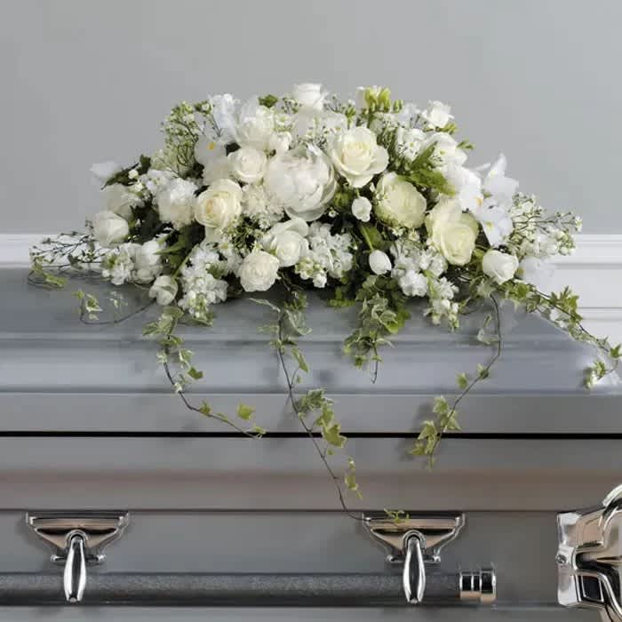 White floral casket spray with trailing ivy on a gray casket