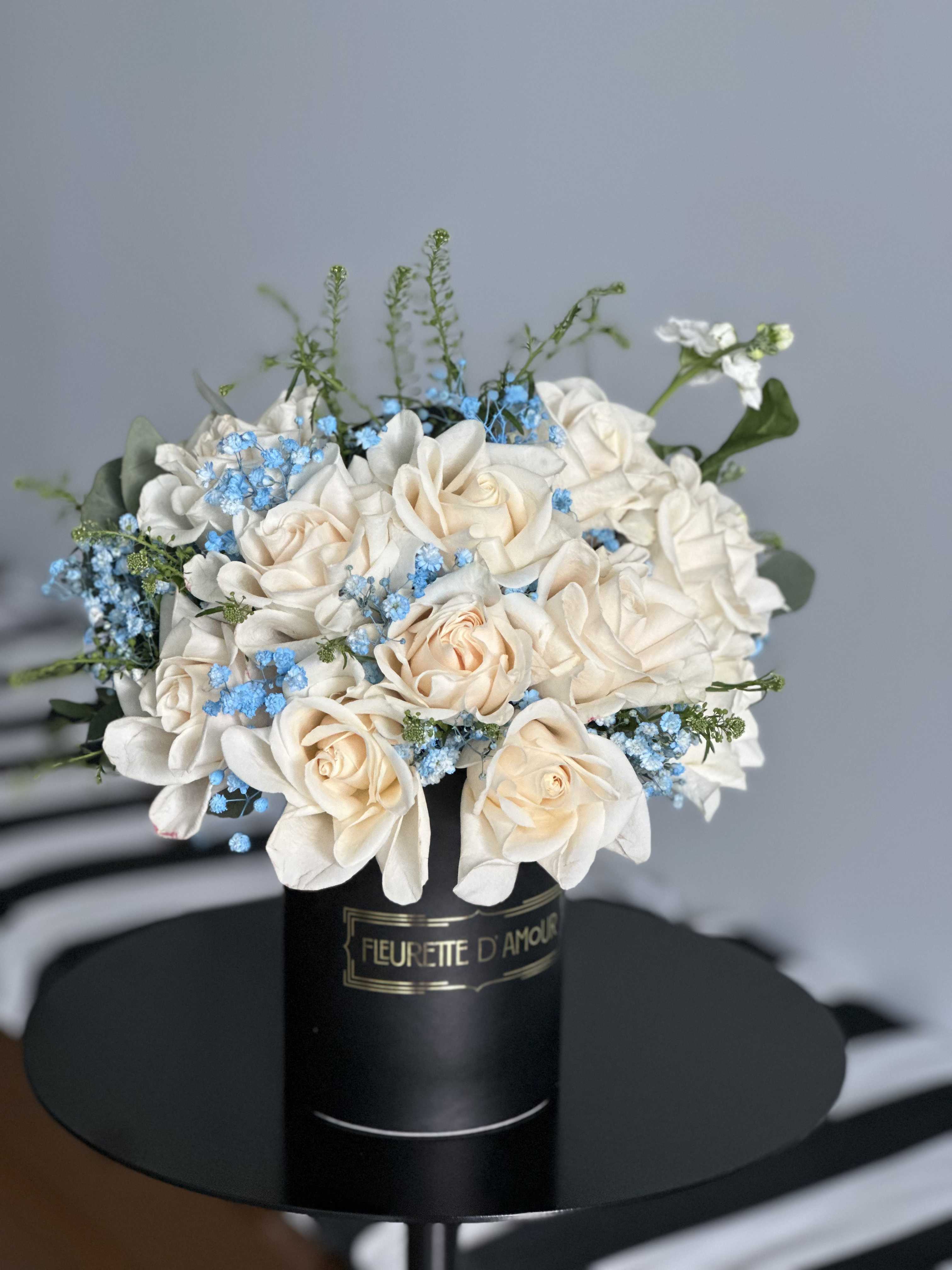 Cream roses and blue filler flowers in a black hatbox