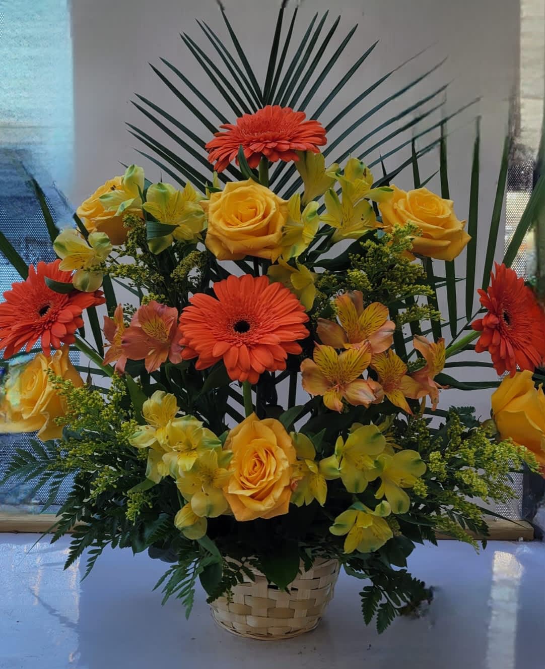 Basket arrangement of orange gerberas, yellow roses, and yellow orchids