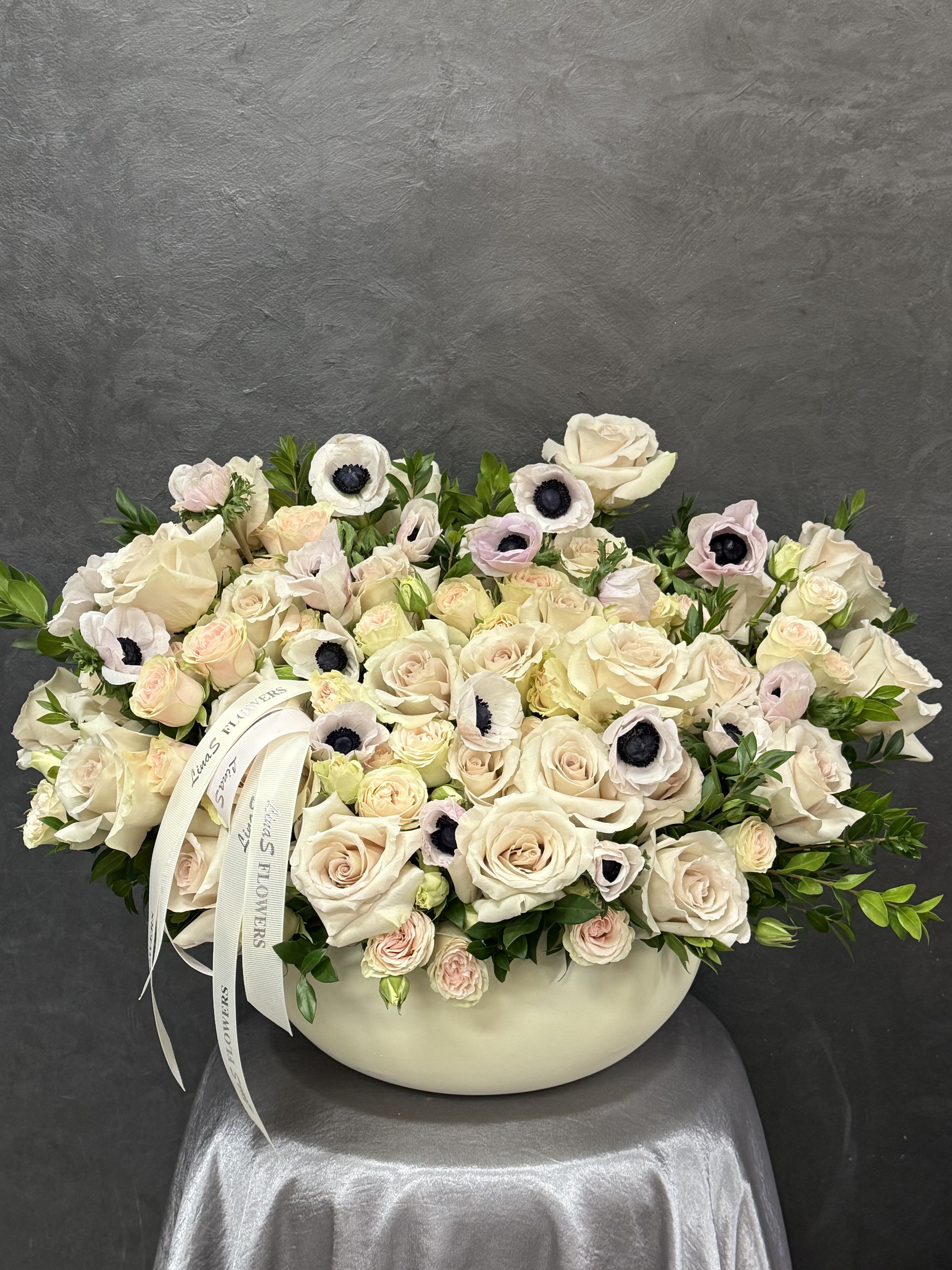 Cream rose arrangement in a low white vase with pale anemones