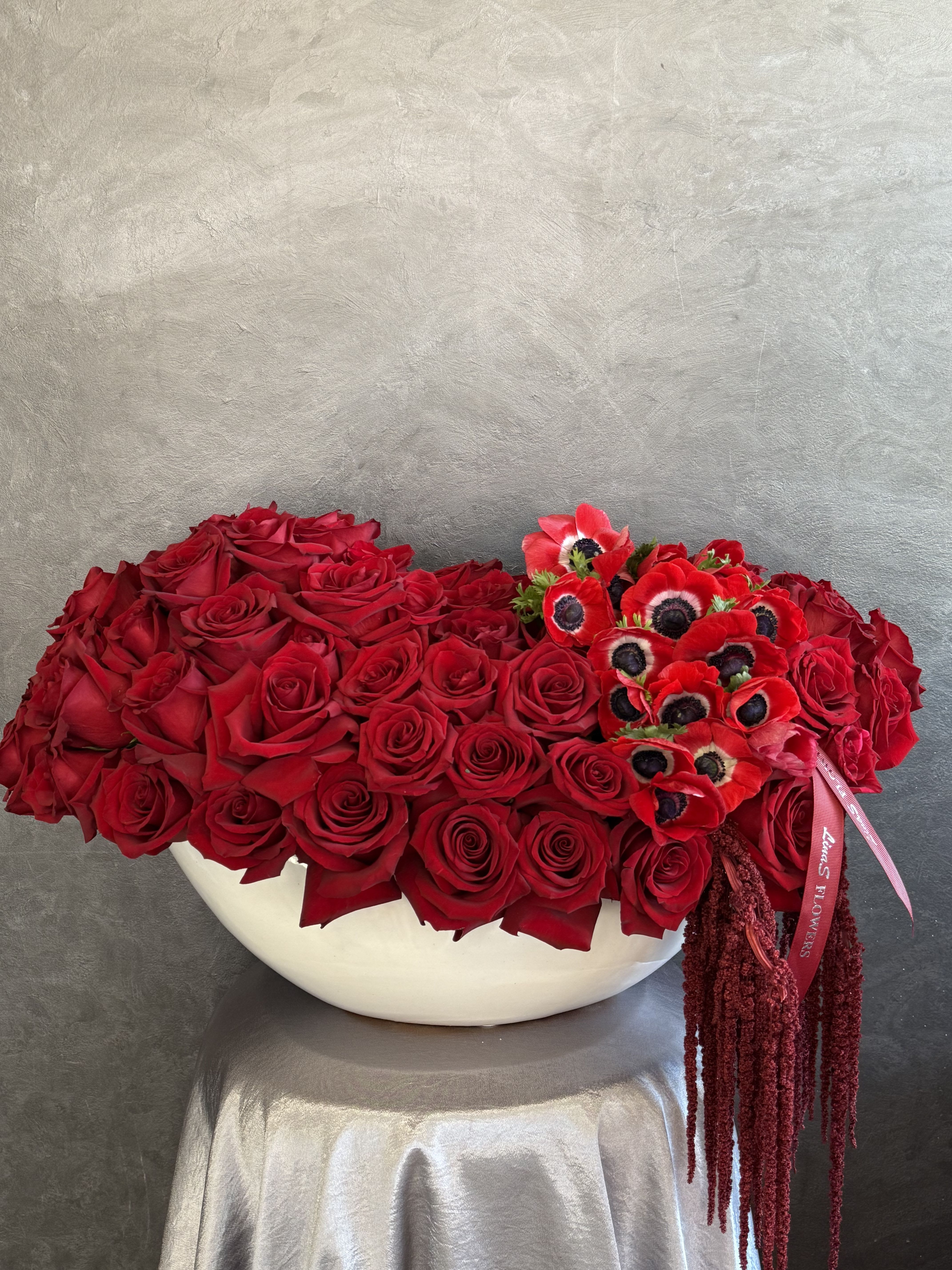 Large red rose arrangement in a white bowl with red anemones