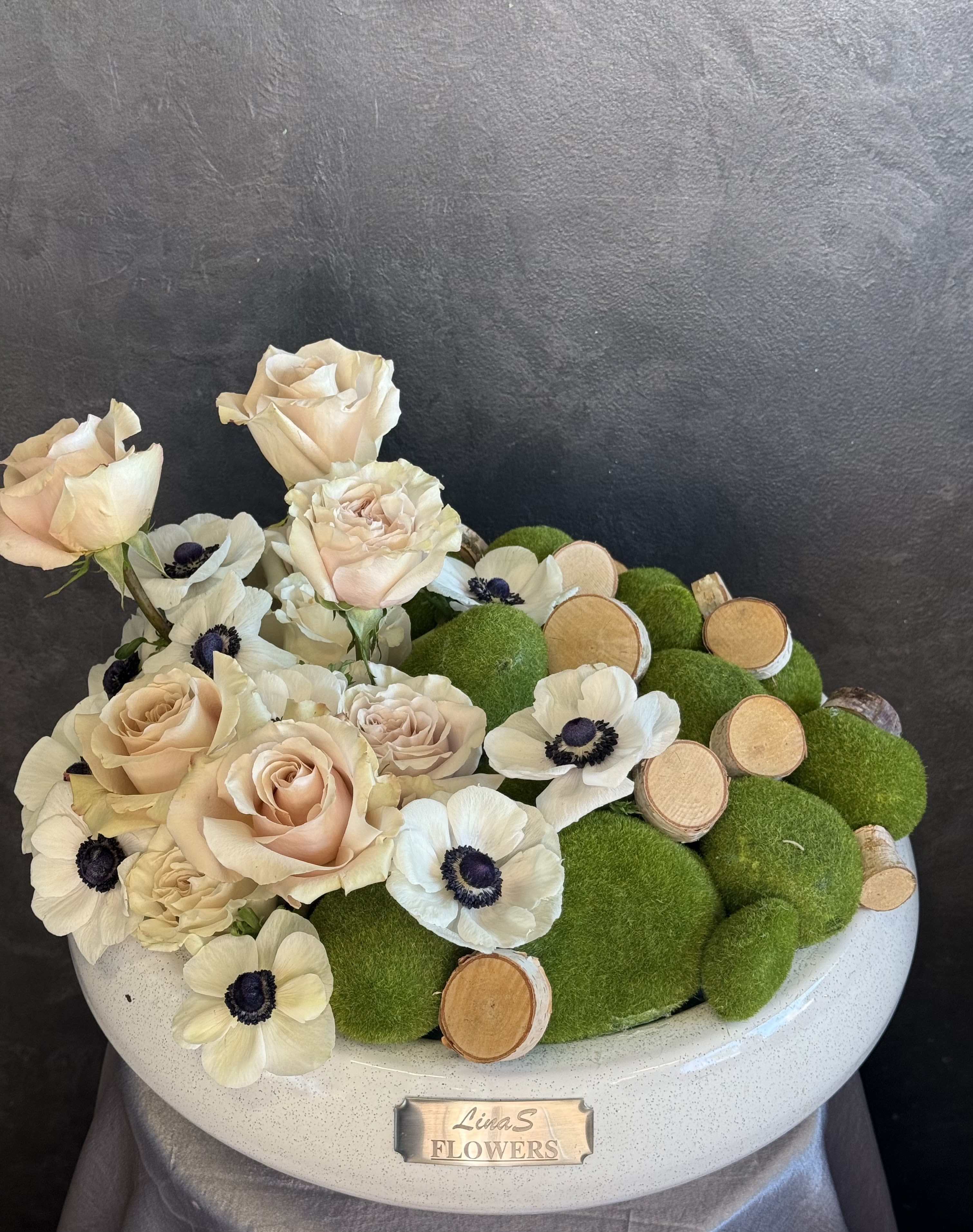 Cream roses and white anemones arranged with green moss balls in a white bowl