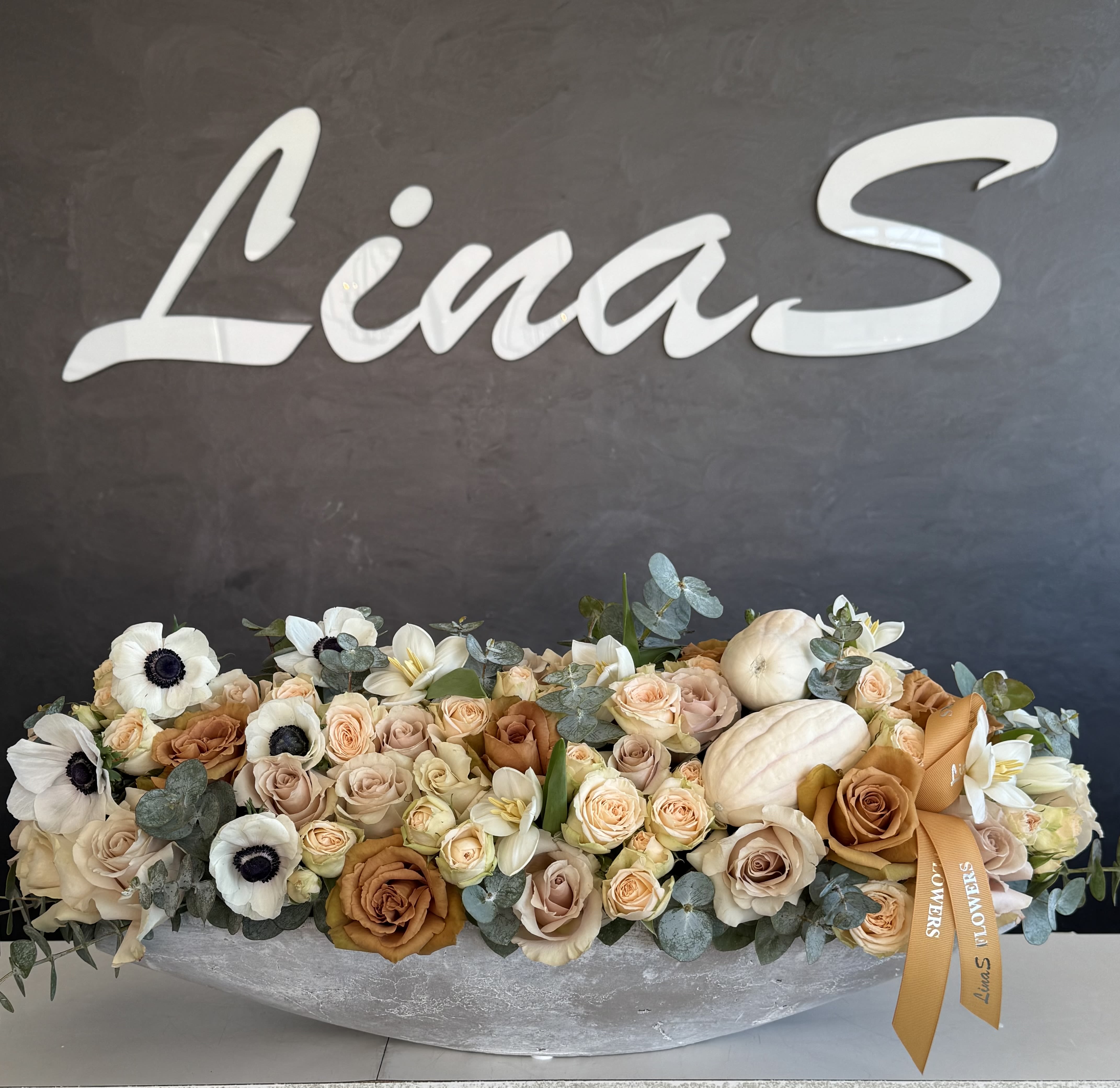 Long low floral arrangement with cream and peach blooms in a silver container