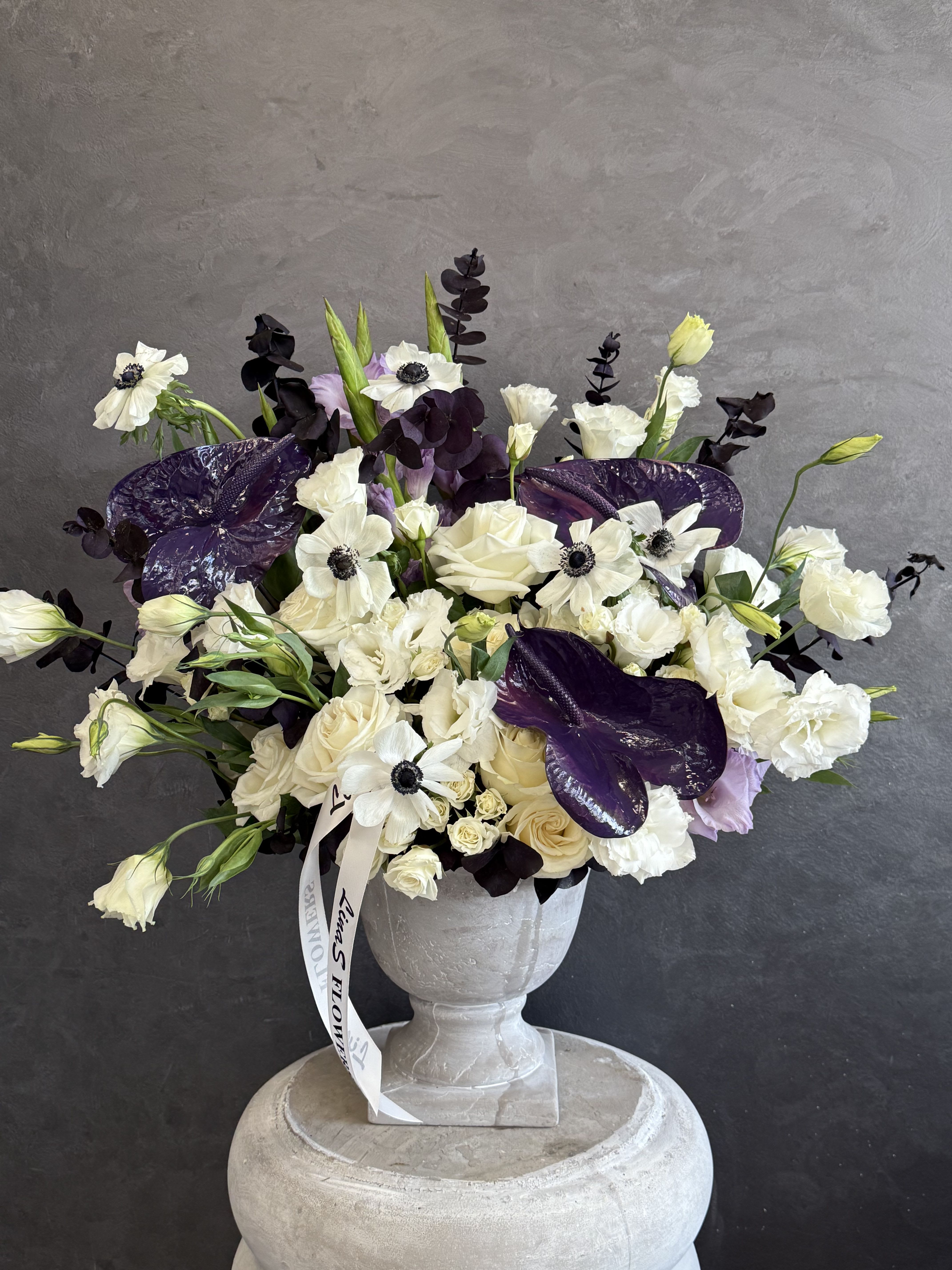 White and purple floral arrangement in a gray urn vase