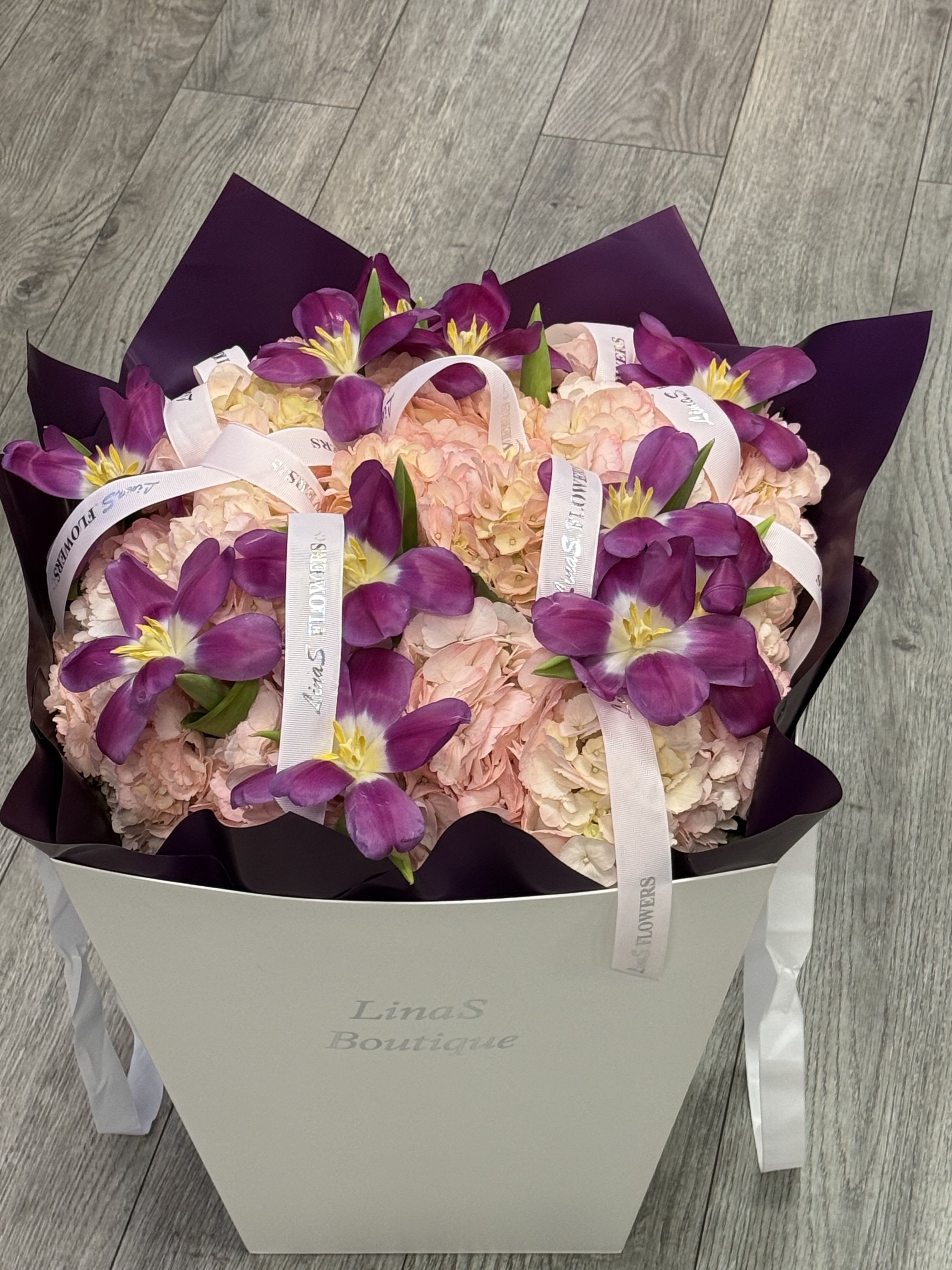 Purple tulips arranged over pale pink hydrangeas in a white box