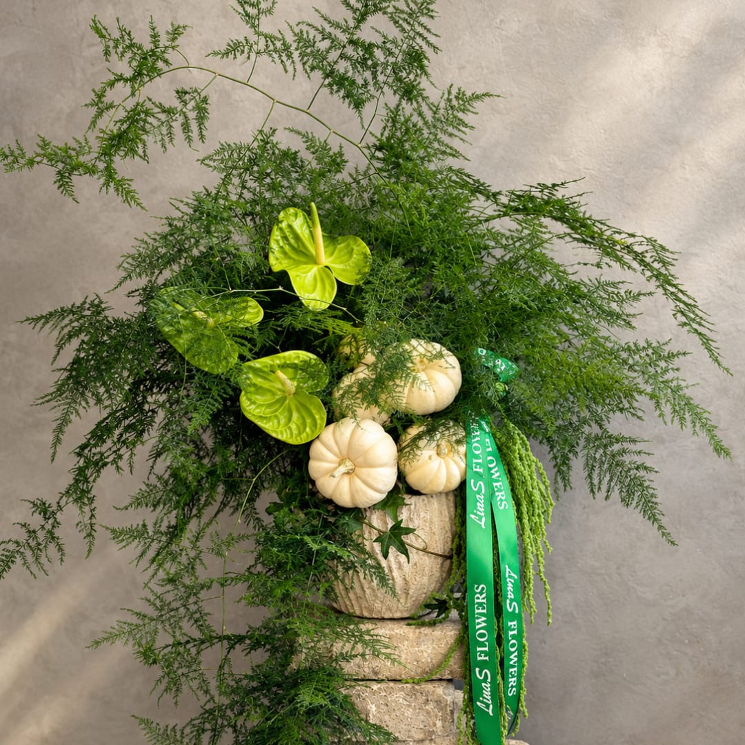 Green foliage arrangement with white mini pumpkins in a textured vase