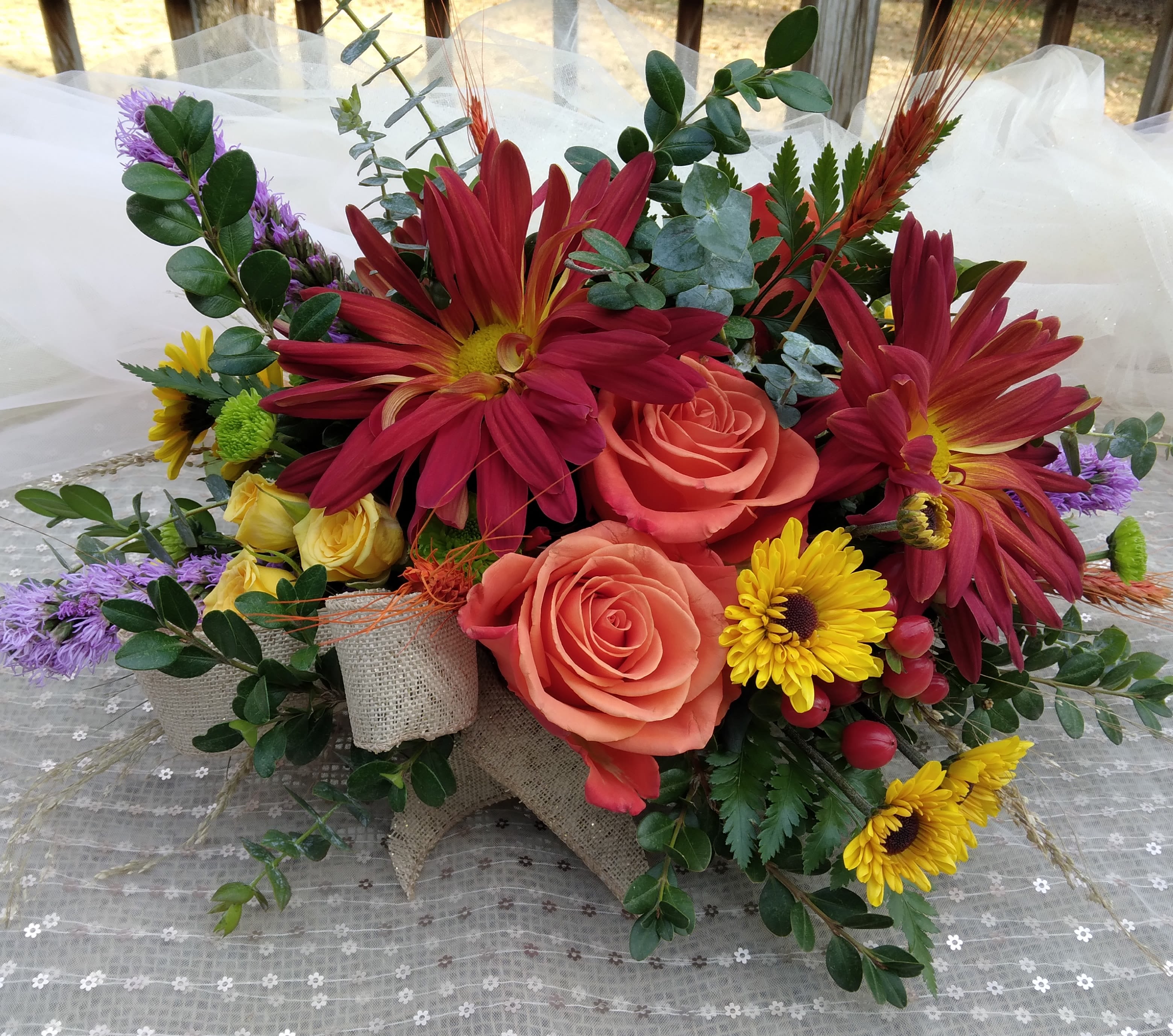 Harvest Equinox (Table Centerpiece) by BloomNation™ - A perfect autumn centerpiece for your dinner party, this arrangement features roses, rovers, fall mums, liatris and assorted, seasonal fall greens and grasses.   Perfect for Thanksgiving, a Halloween dinner, or Rosh Hashanah.  The Standard size is a round centerpiece.  The Deluxe and Premium size options are long &amp; low centerpieces with the premium containing 2 candles.    
