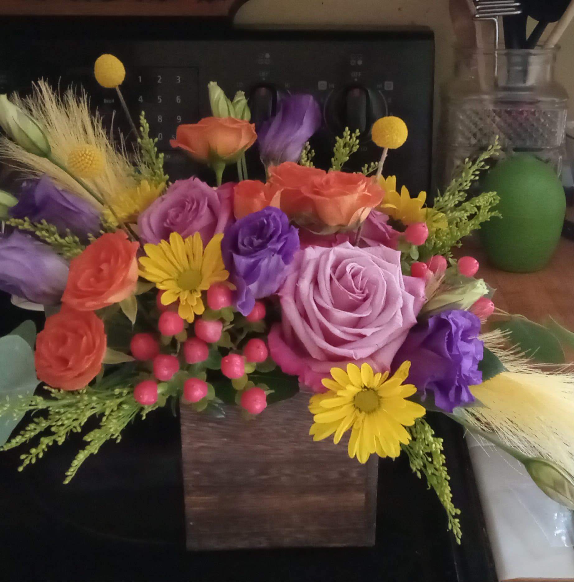 Vibrant Variety by BloomNation™ - A trendy, wooden box filled with purple roses, lisianthus, orange spray roses, craspedia balls, hypericum berries, yellow daisies and a few artificial pretties for that WOW factor!this arrangement is seeking a comfortable home. It is willing to impress, please, and WOW your recipient. This bright and vivid variety is appropriate for all occasions. Send some their WoW their way today!