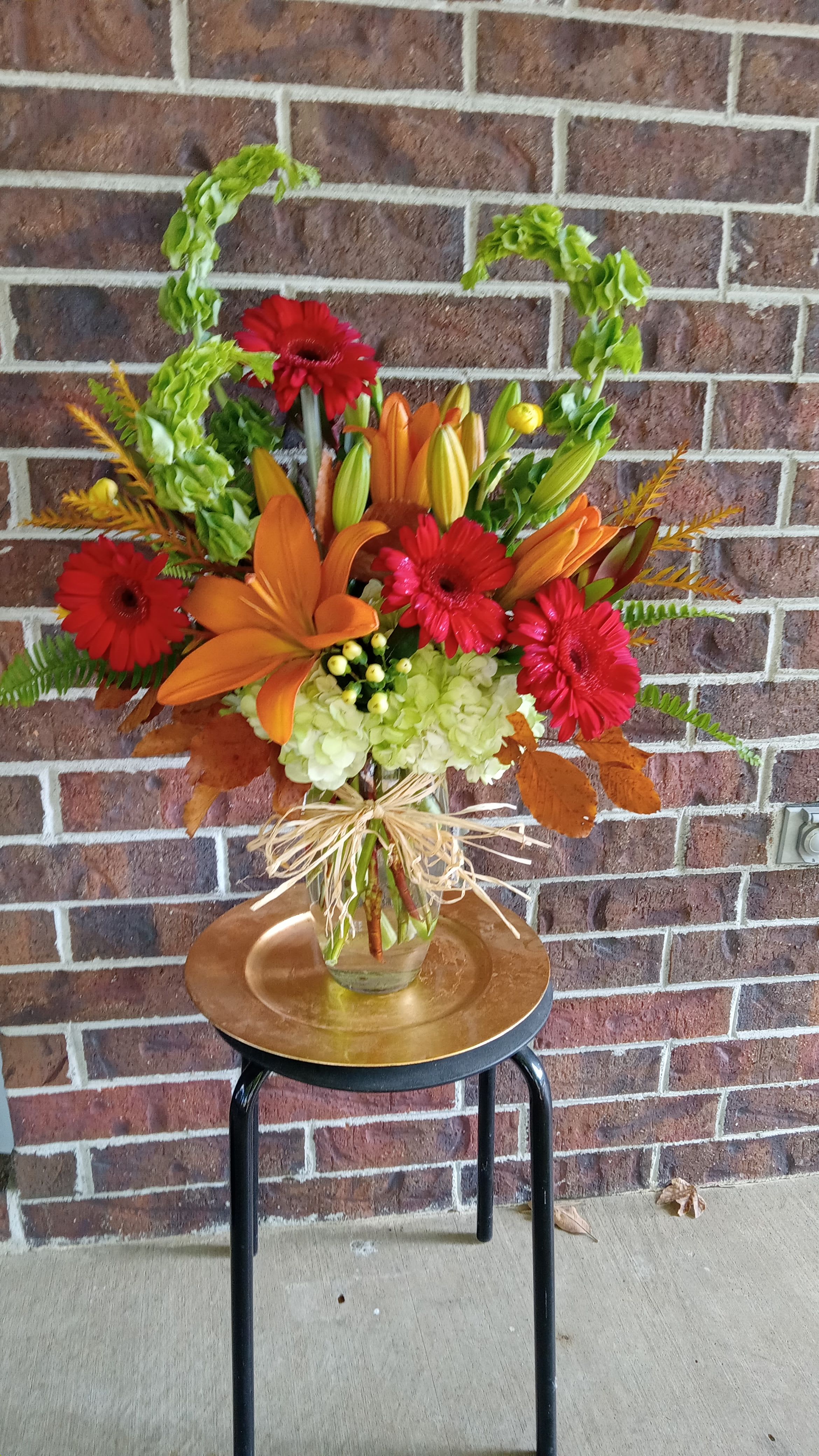 Buenos Dias by BloomNation™ - Rise and shine with this tall and bright arrangement. Tall reaching daisies, bells of Ireland and lilies in bright orange and green make this arrangement pop. Perfect for Cinco De Mayo, wishing somebody a happy birthday or welcoming a new baby.   APPROXIMATE DIMENSIONS 16" W X 31" H  