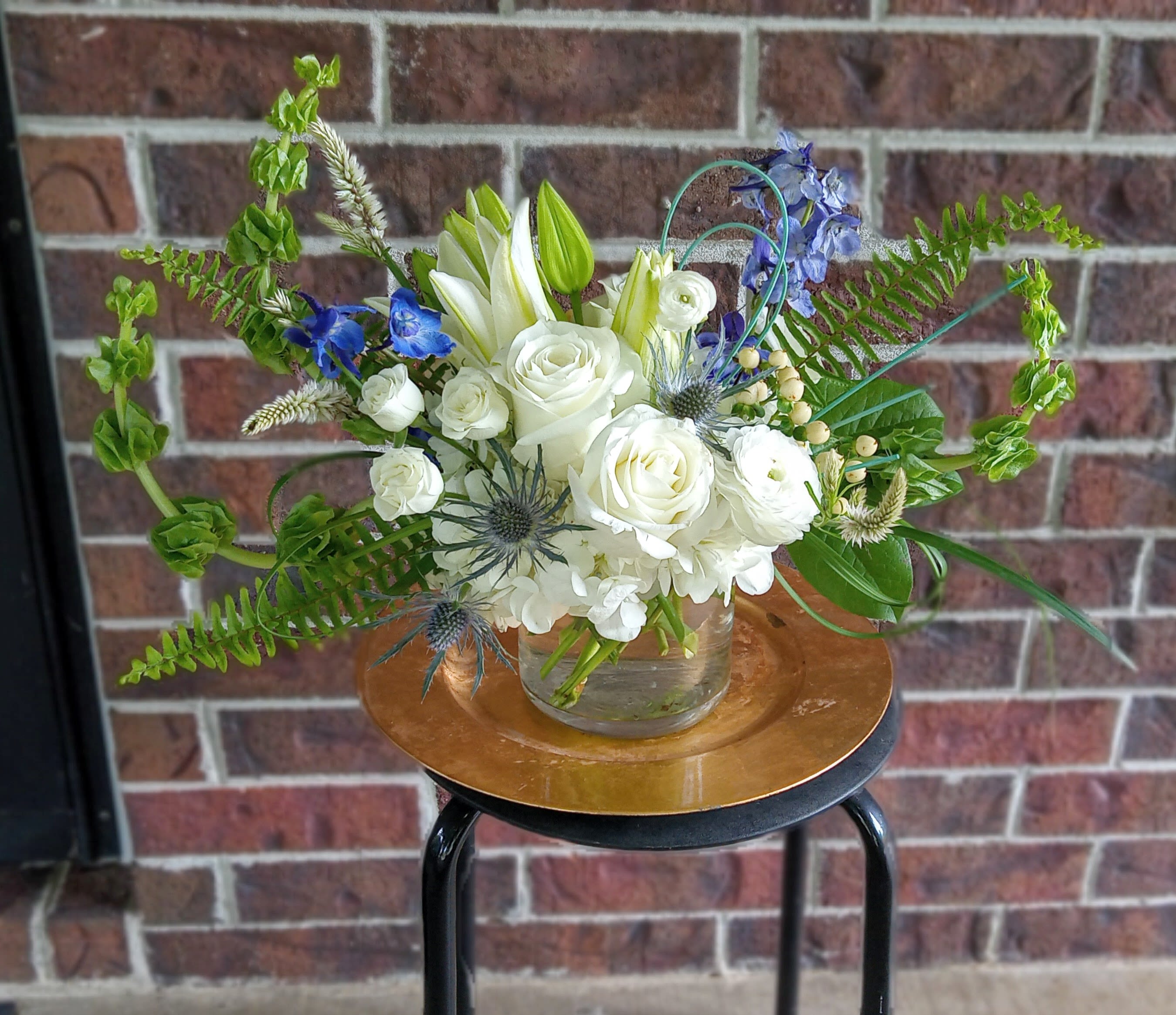 Purity by BloomNation™ - This arrangement contains white ranunculus, hydrangea, belles of Ireland, roses, tulips, stock, and other seasonal blooms. Perfect for sympathy, memorial or funeral service.  ** Premium size option is pictured **