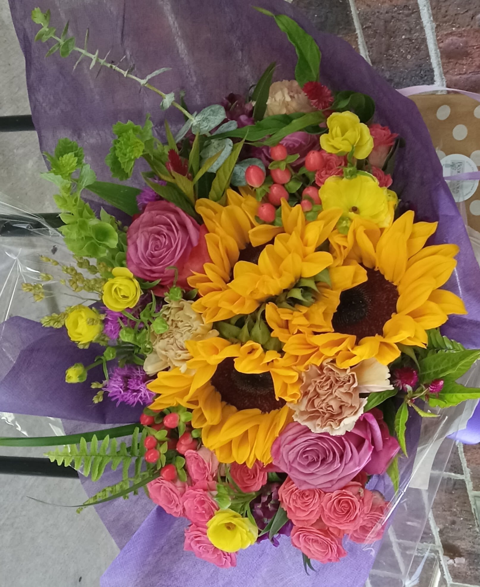 Bouquet with sunflowers, roses, and carnations wrapped in purple paper