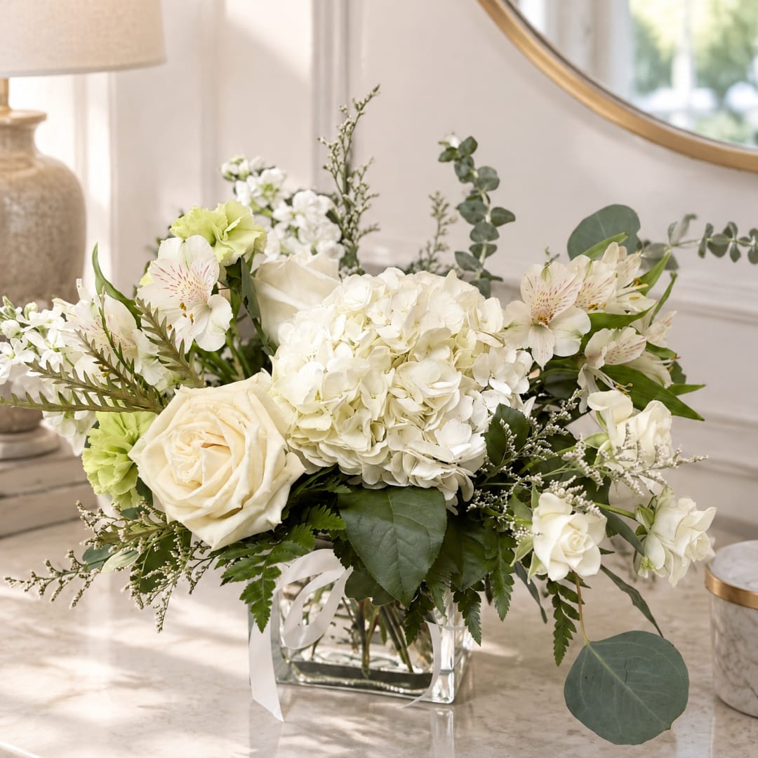 White floral arrangement in a clear glass vase with roses and hydrangeas