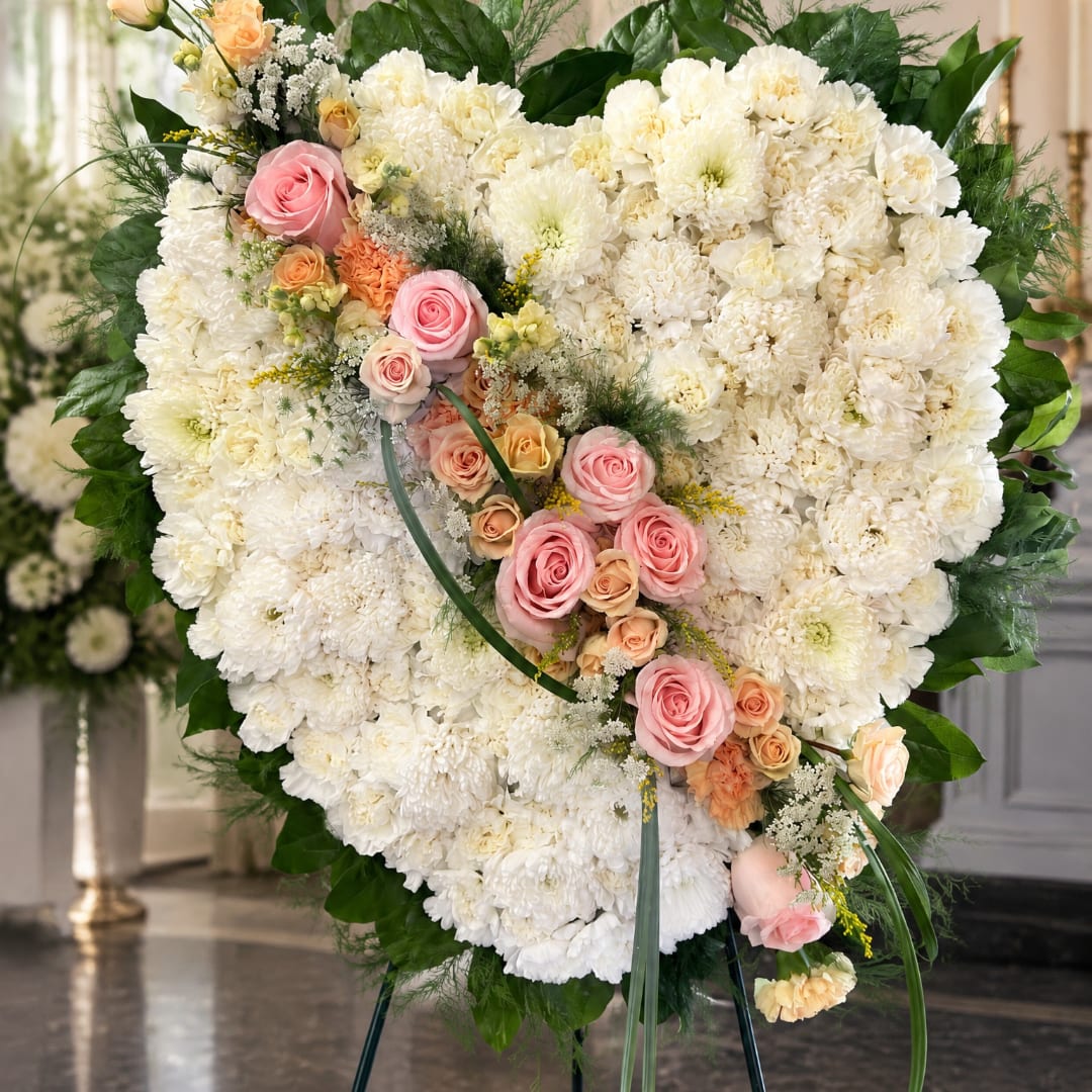 Heart-shaped white floral standing spray with pink roses and peach accents
