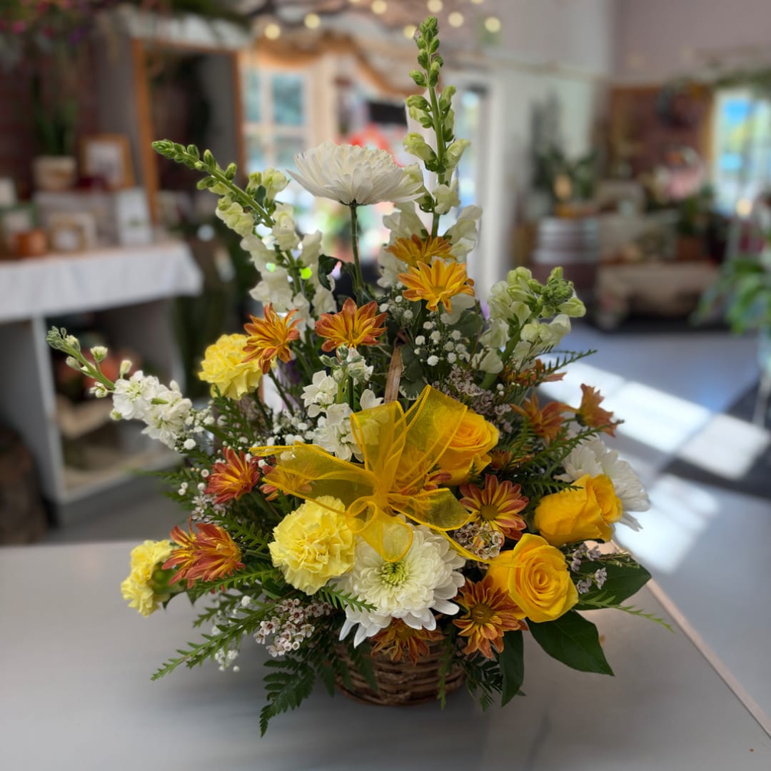 Mixed yellow and white flower arrangement in a wicker basket with a yellow bow