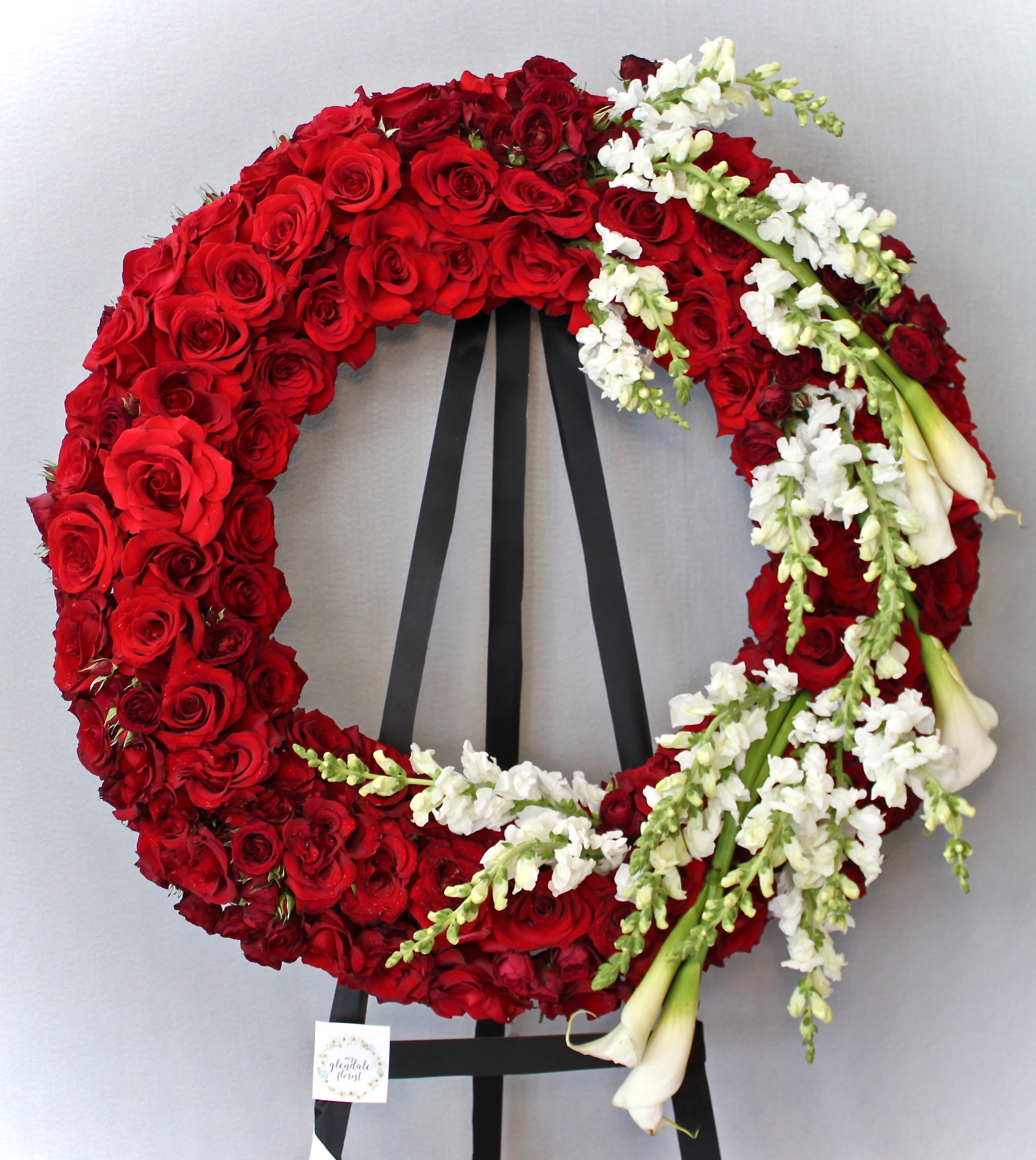Red Rose Romance Wreath  - Covered in red roses, this wreath also includes calla lilies and snapdragons.     We include easel, printed banner and delivery (some fees may apply).    Standard size is 30'', deluxe is 36'', and premium is 42''.