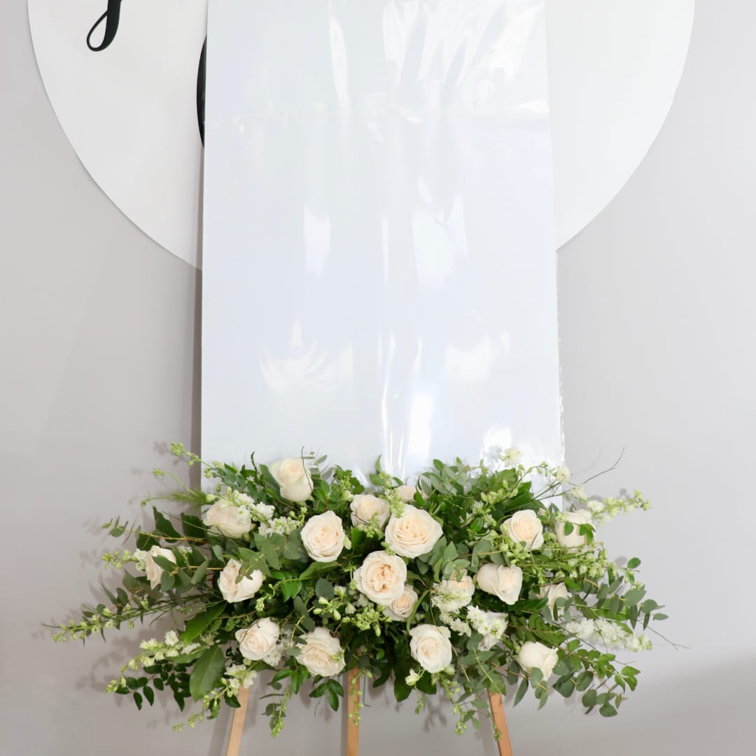 White rose arrangement on a wooden easel with greenery