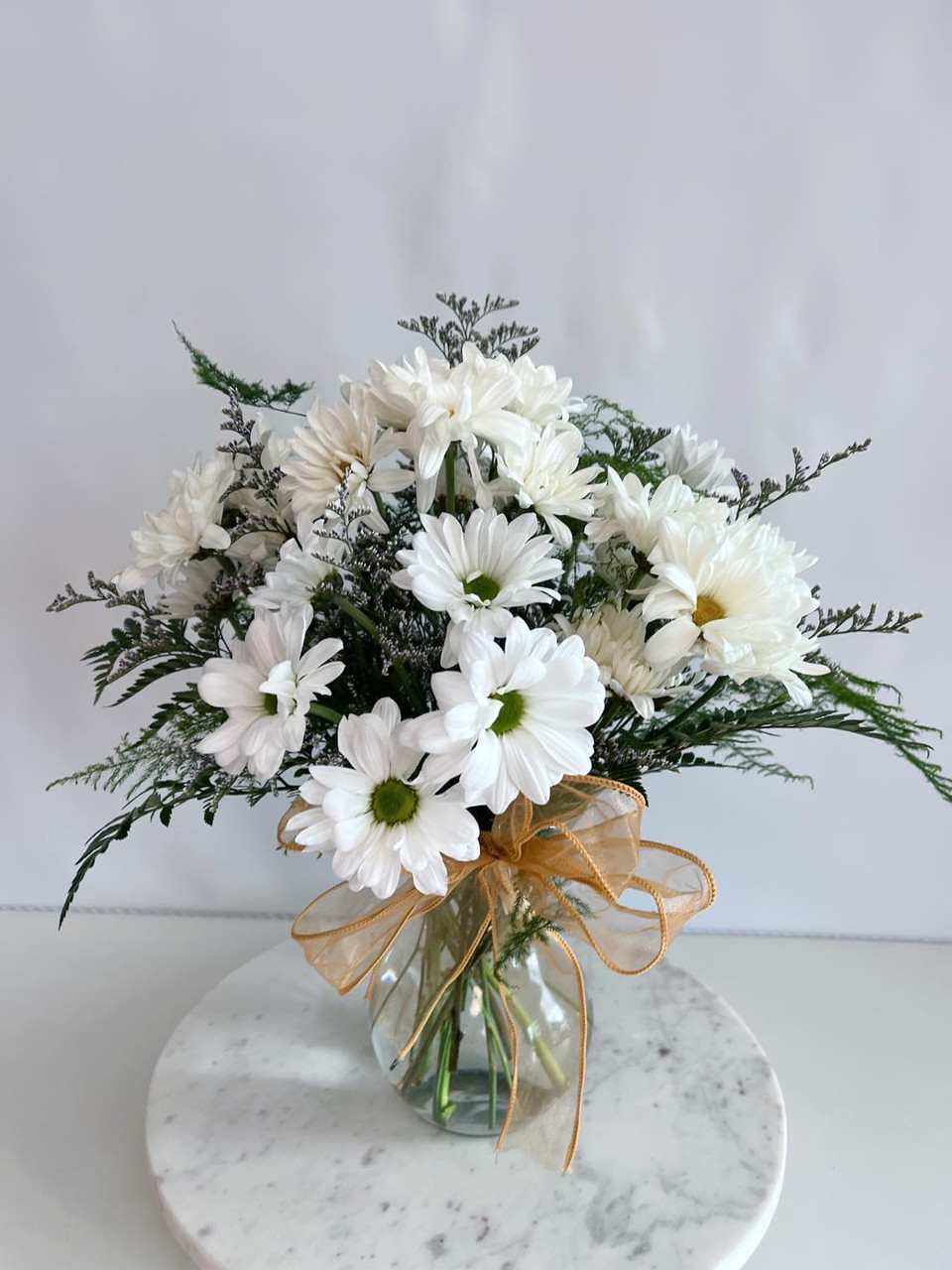 White daisy bouquet in a glass vase with a gold ribbon