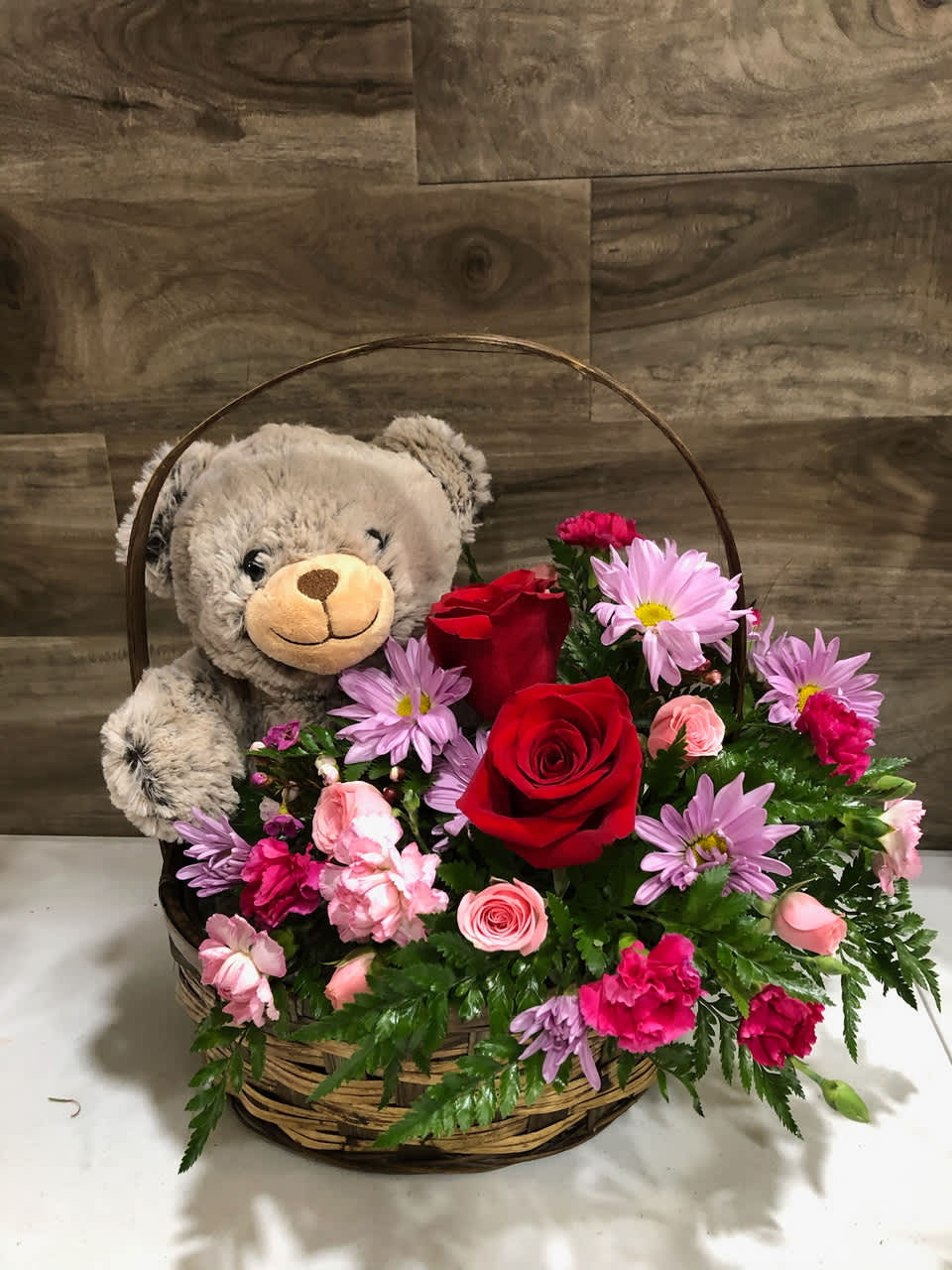 Teddy bear in a basket with red roses and pink flowers