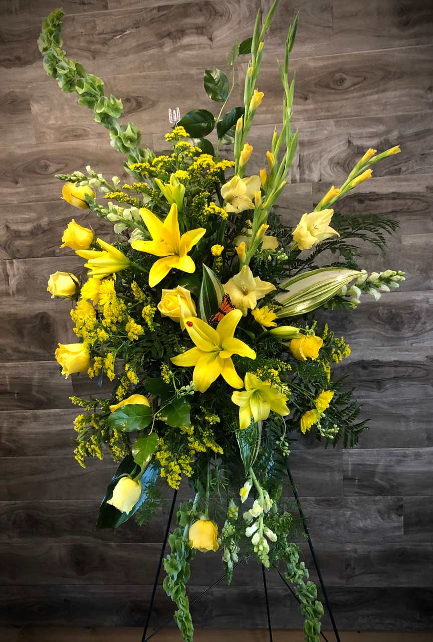 Tall yellow floral standing spray with lilies and roses on a black easel