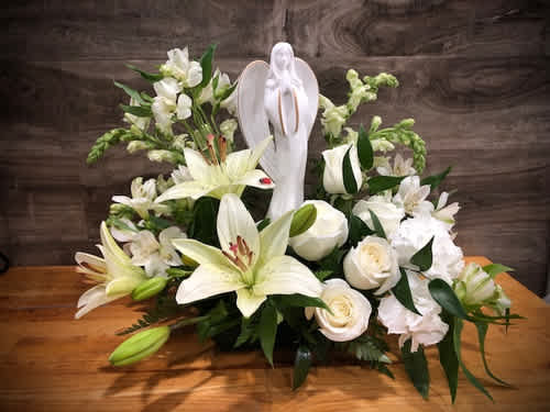 White lilies and roses arranged around a white angel figurine