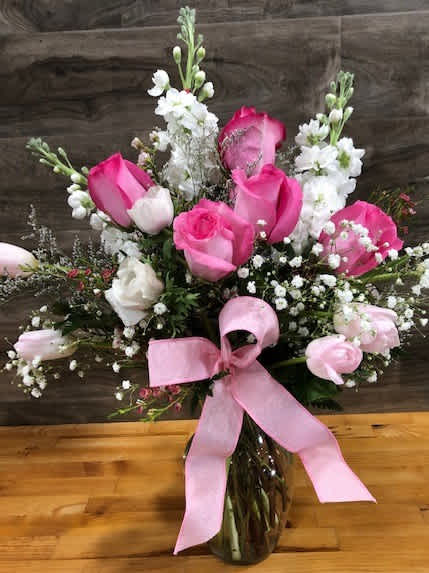 Pink and white rose bouquet in a glass vase with a pink ribbon