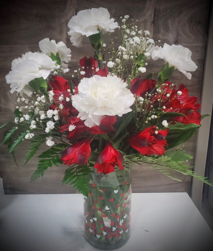 Red and white carnations in a clear heart-patterned vase