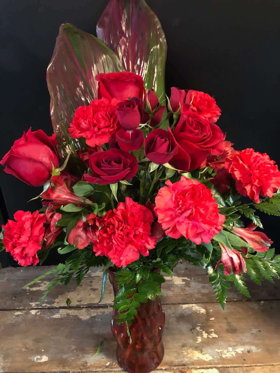 Red roses and carnations arranged in a vase with tropical leaves