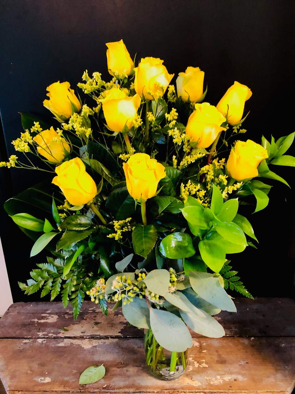Yellow roses arranged in a clear glass vase with mixed greenery