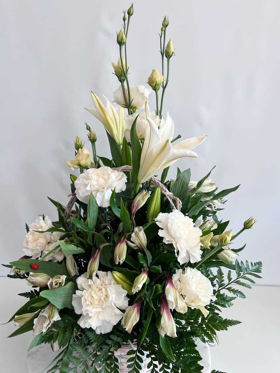 White lilies and carnations arranged in a basket with greenery
