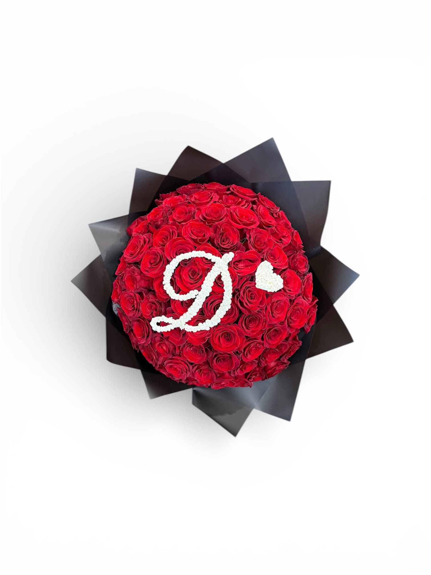 Round bouquet of red roses with white flowers forming a letter D and heart, wrapped in black paper.