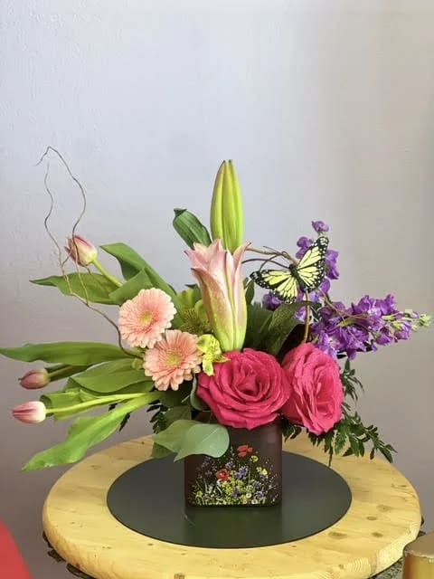 Pink roses and lilies in a square vase with a butterfly accent