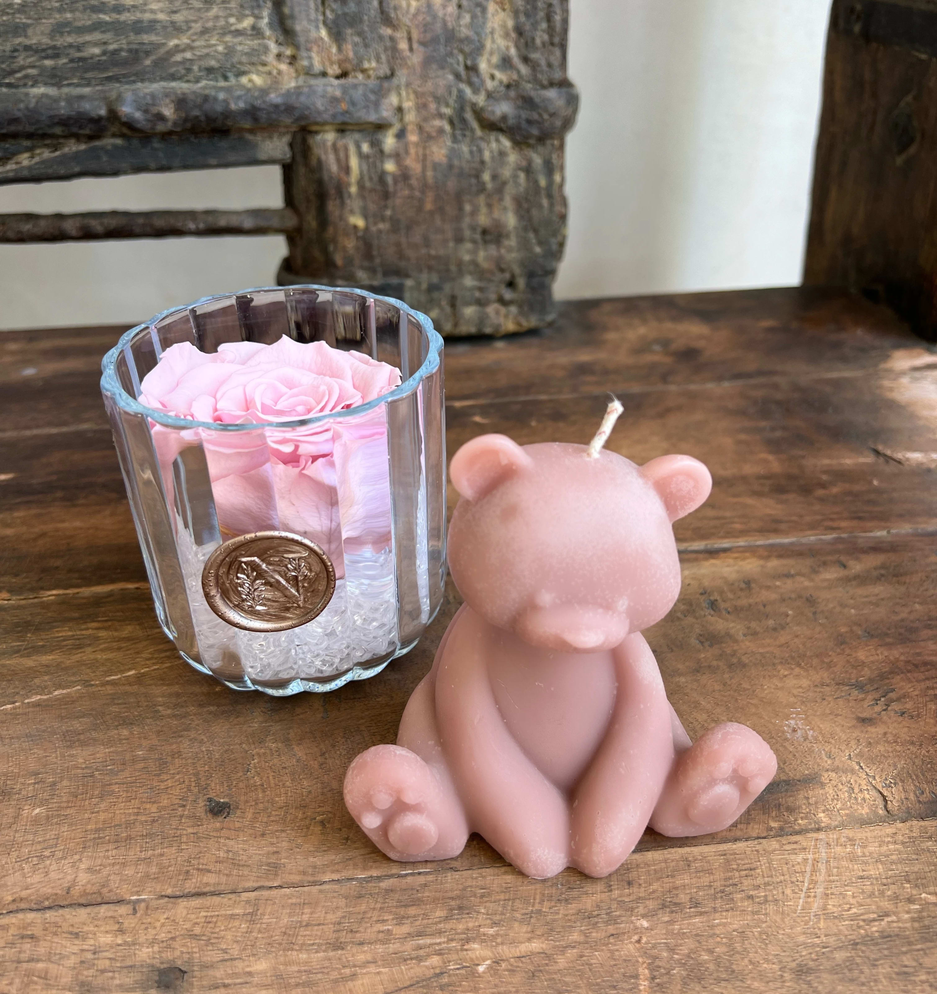 Pink rose in a glass votive beside a pink bear-shaped candle