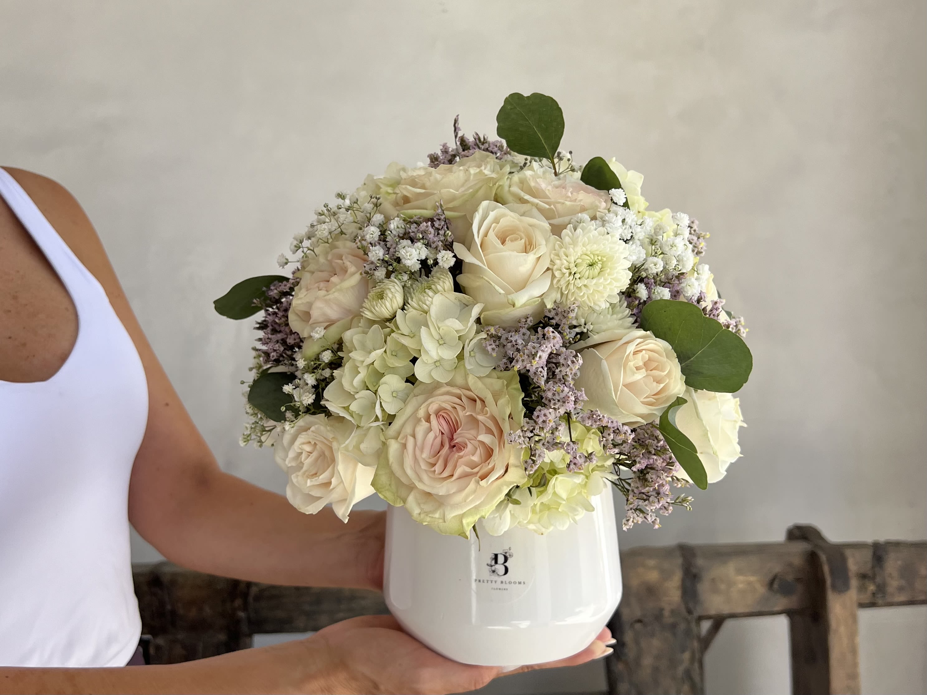 Cream roses and hydrangeas in a white vase with green leaves