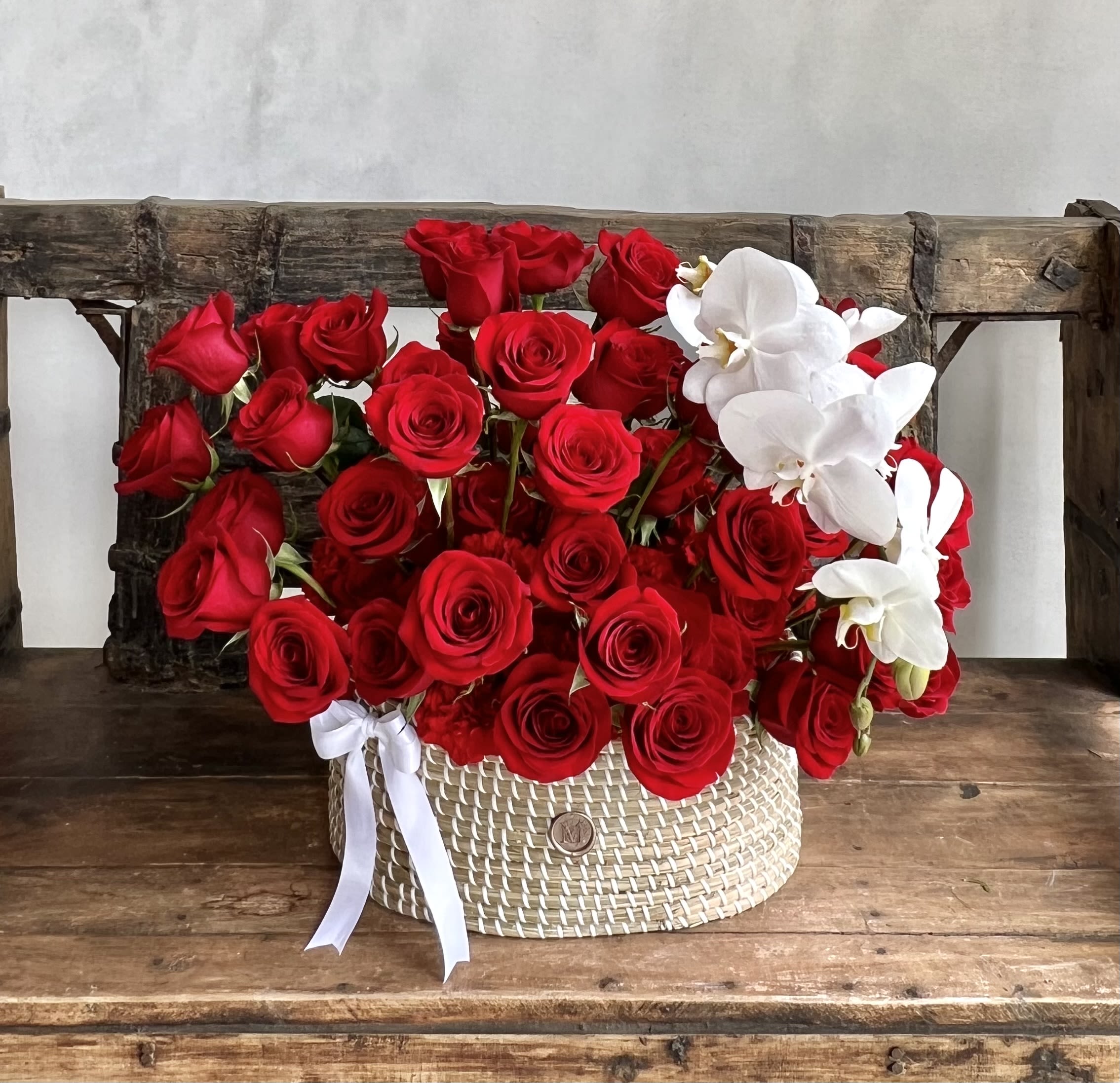 Red roses and white orchids arranged in a woven basket with a white ribbon