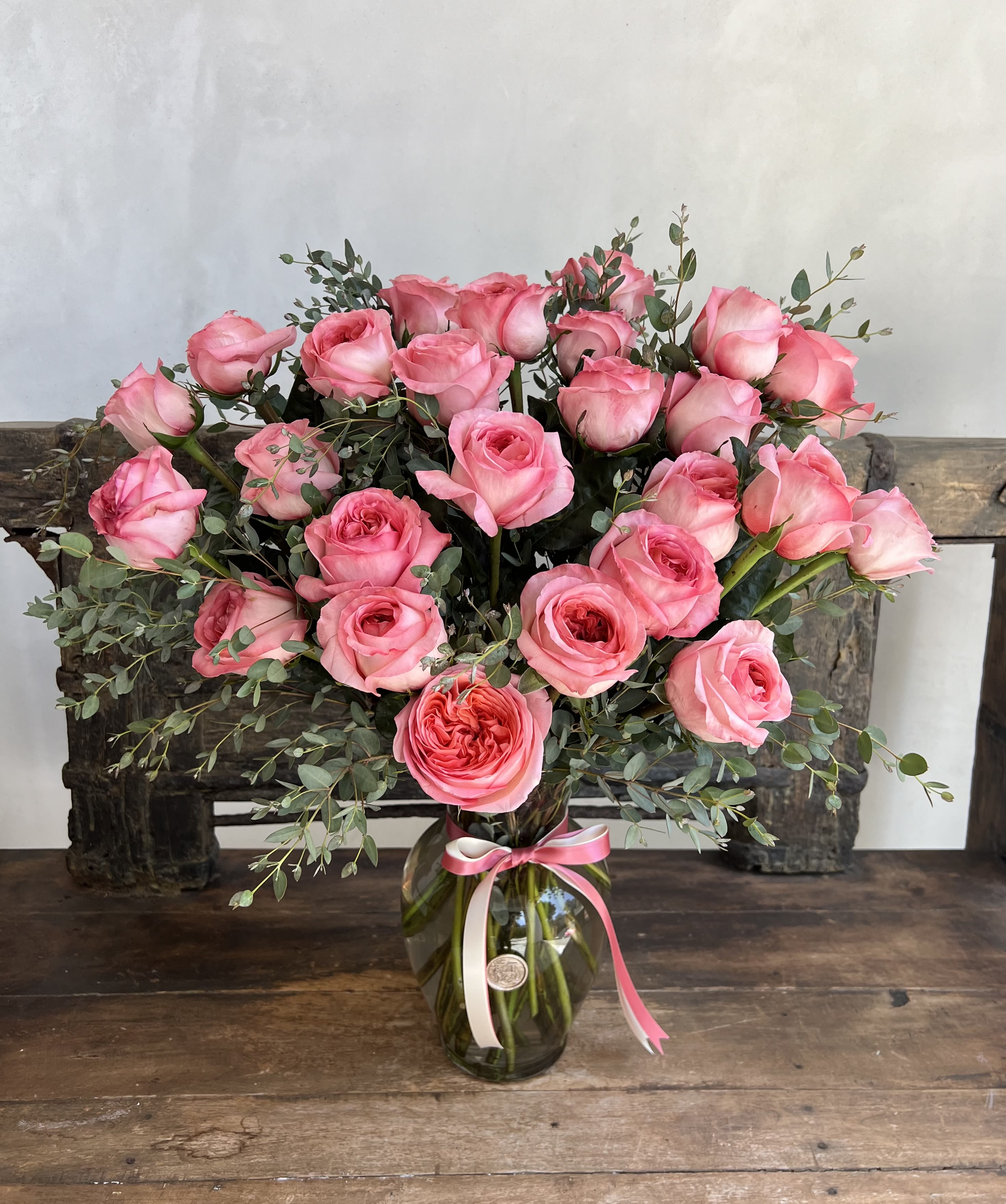 Pink roses arranged in a glass vase with a ribbon