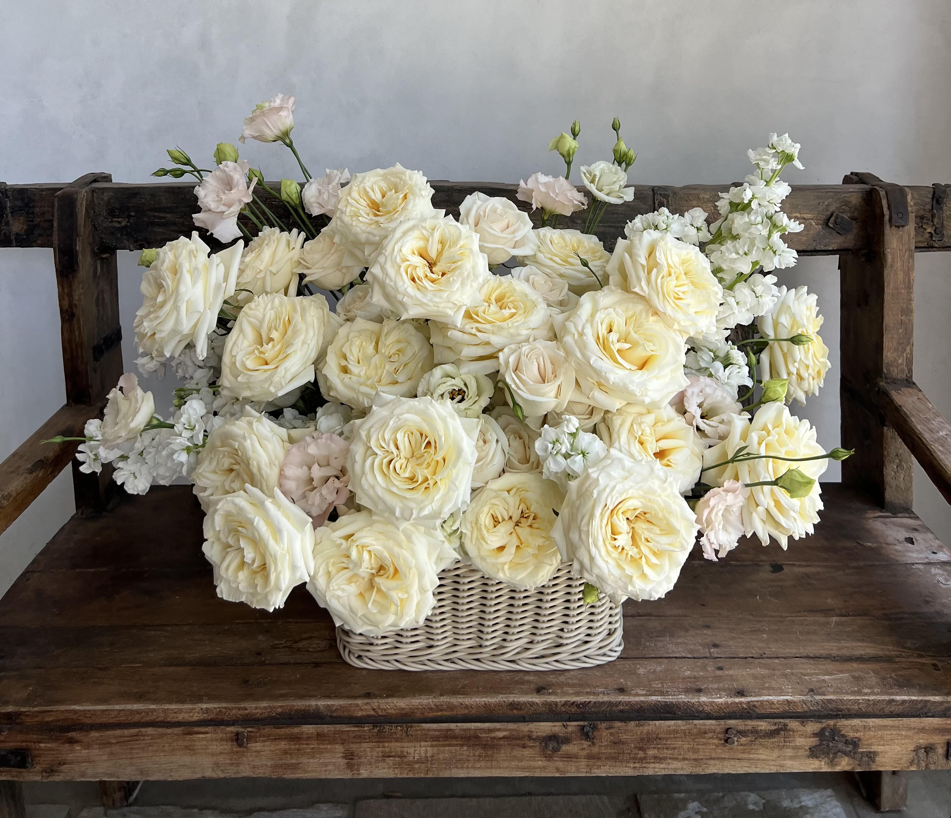 Cream roses and white blooms arranged in a wicker basket