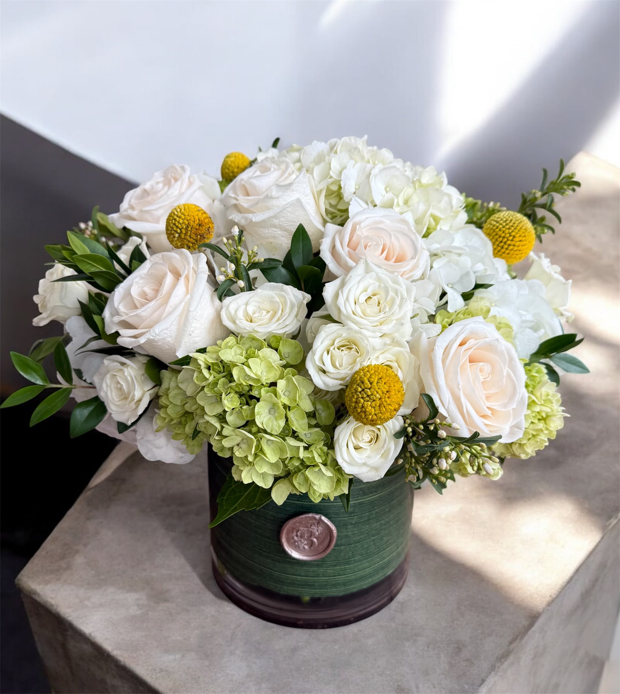 White roses and hydrangeas in a green round box with yellow accents