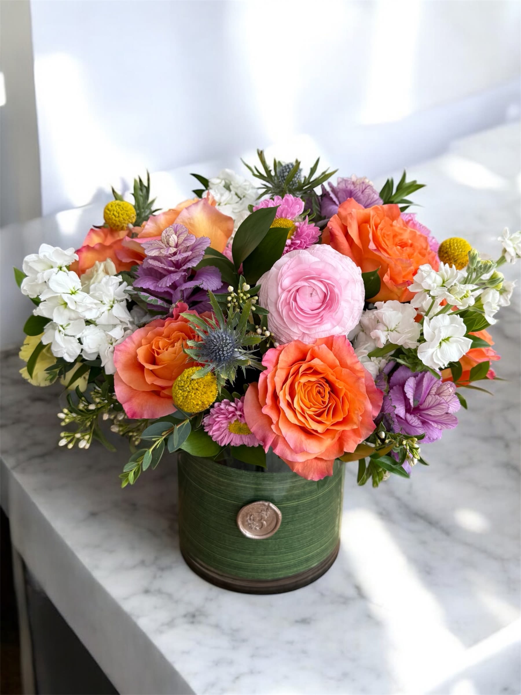 Colorful bouquet of roses, ranunculus, and white blooms in a green container