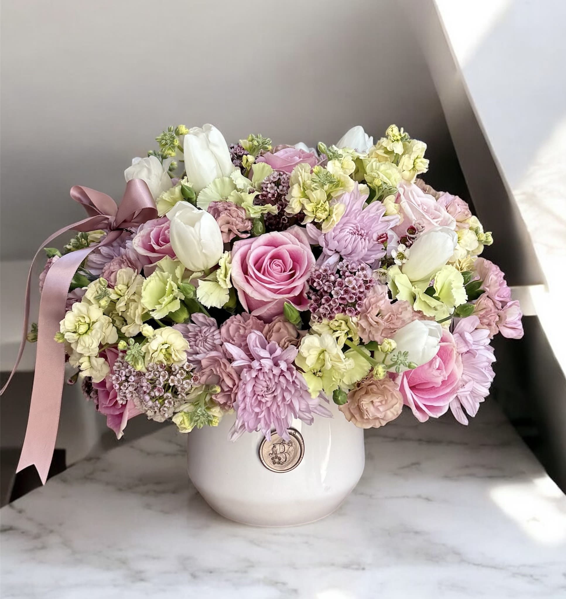 Pink and white mixed flower arrangement in a white vase with a ribbon