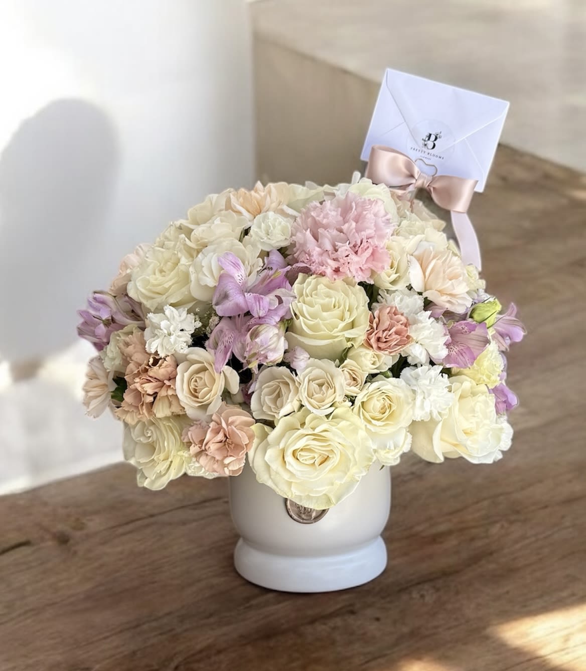 Pastel bouquet of roses and carnations in a white vase with a ribboned card