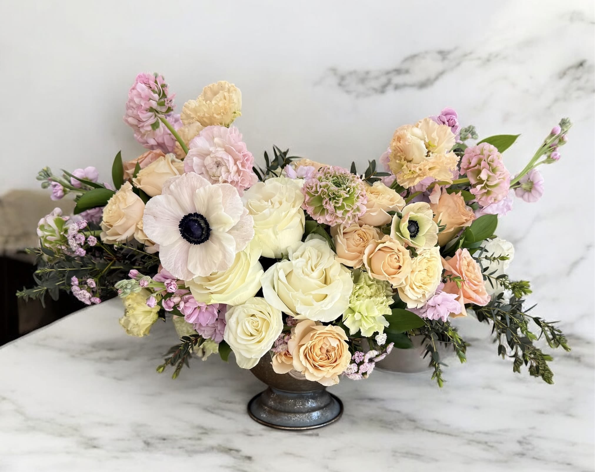 Pastel floral arrangement in a low pedestal vase with roses and anemones