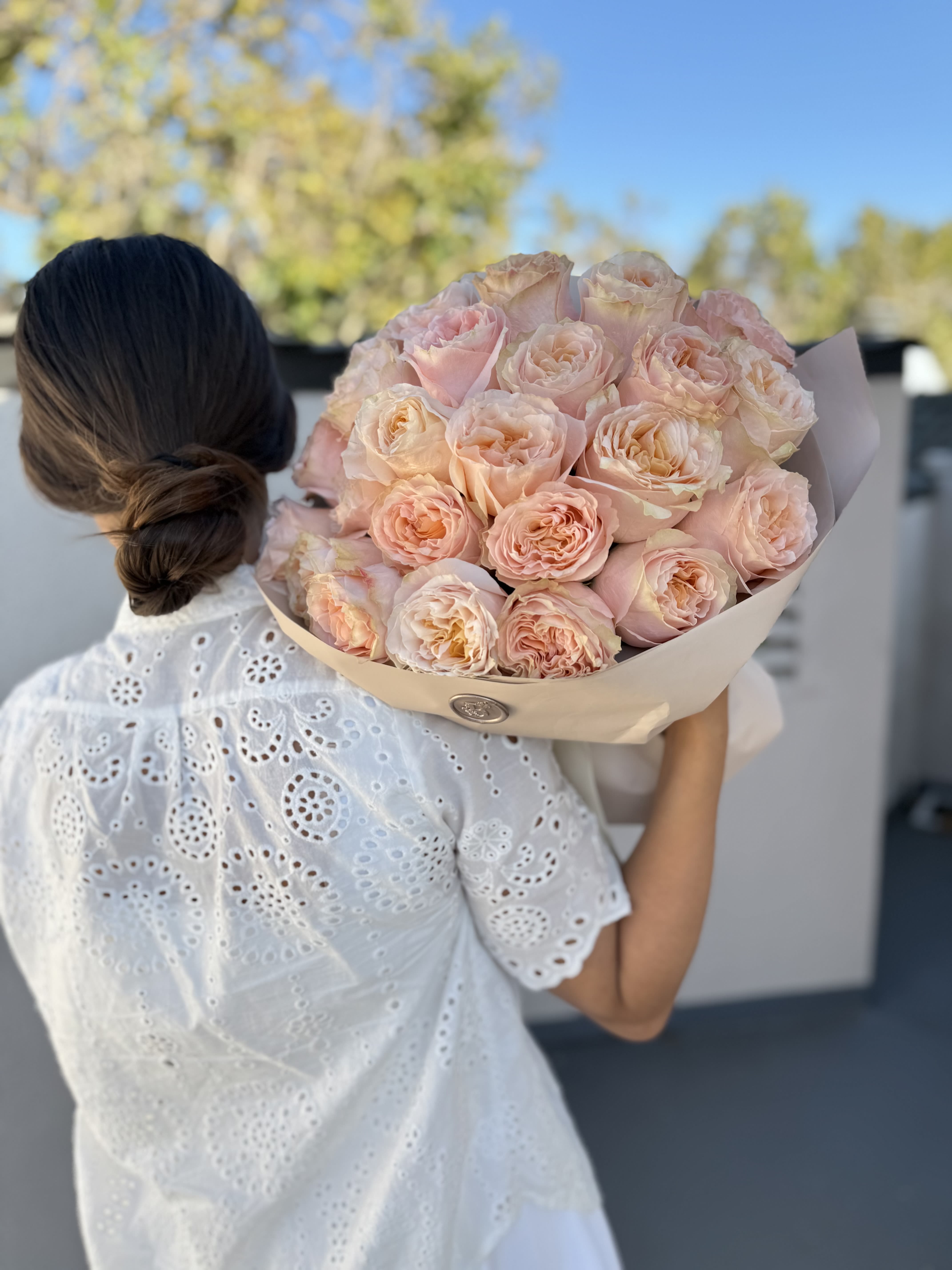 Woman holding a bouquet of pale pink roses wrapped in beige paper