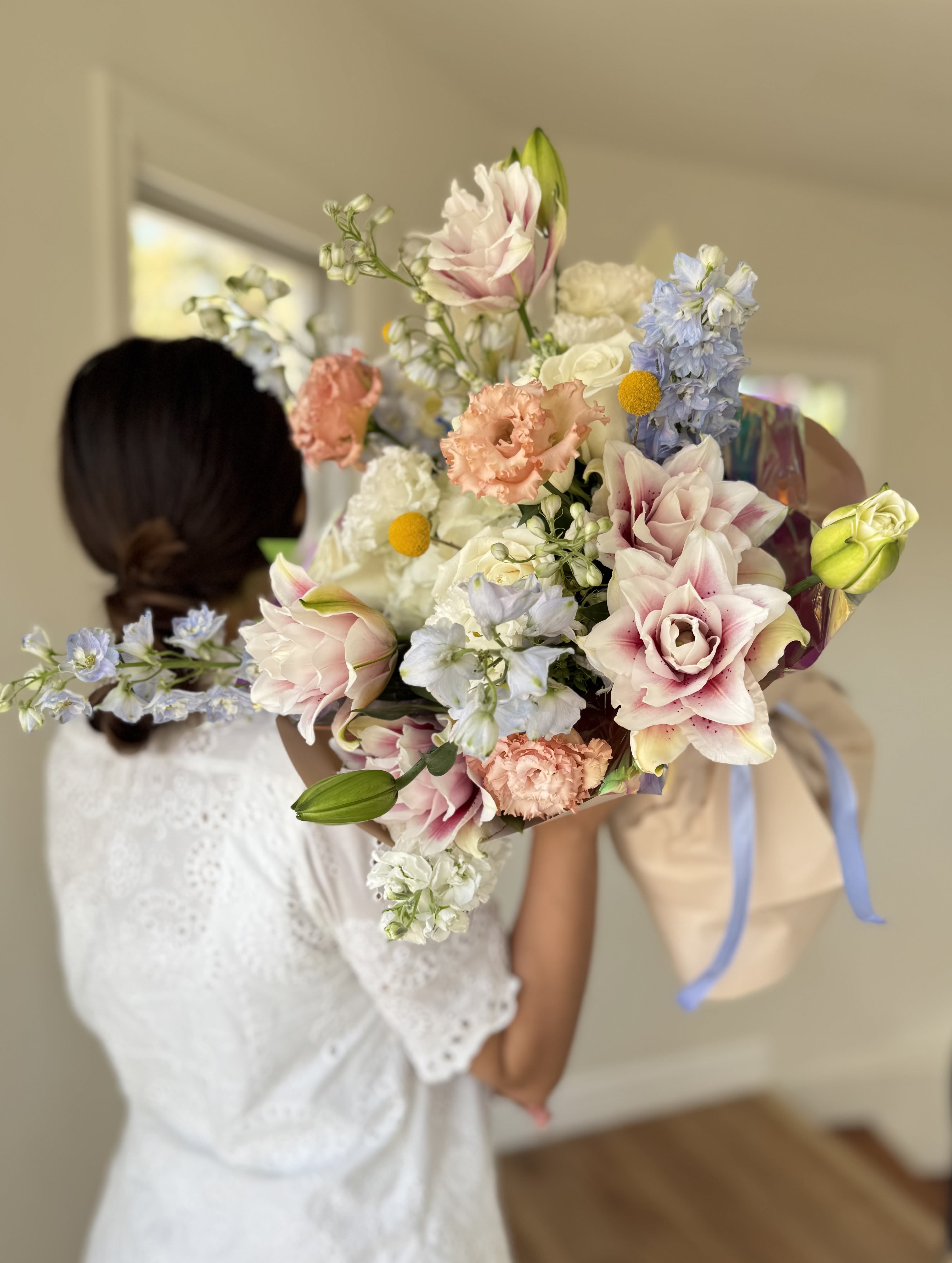 Bride holding a pastel bouquet with lilies, roses, and blue flowers
