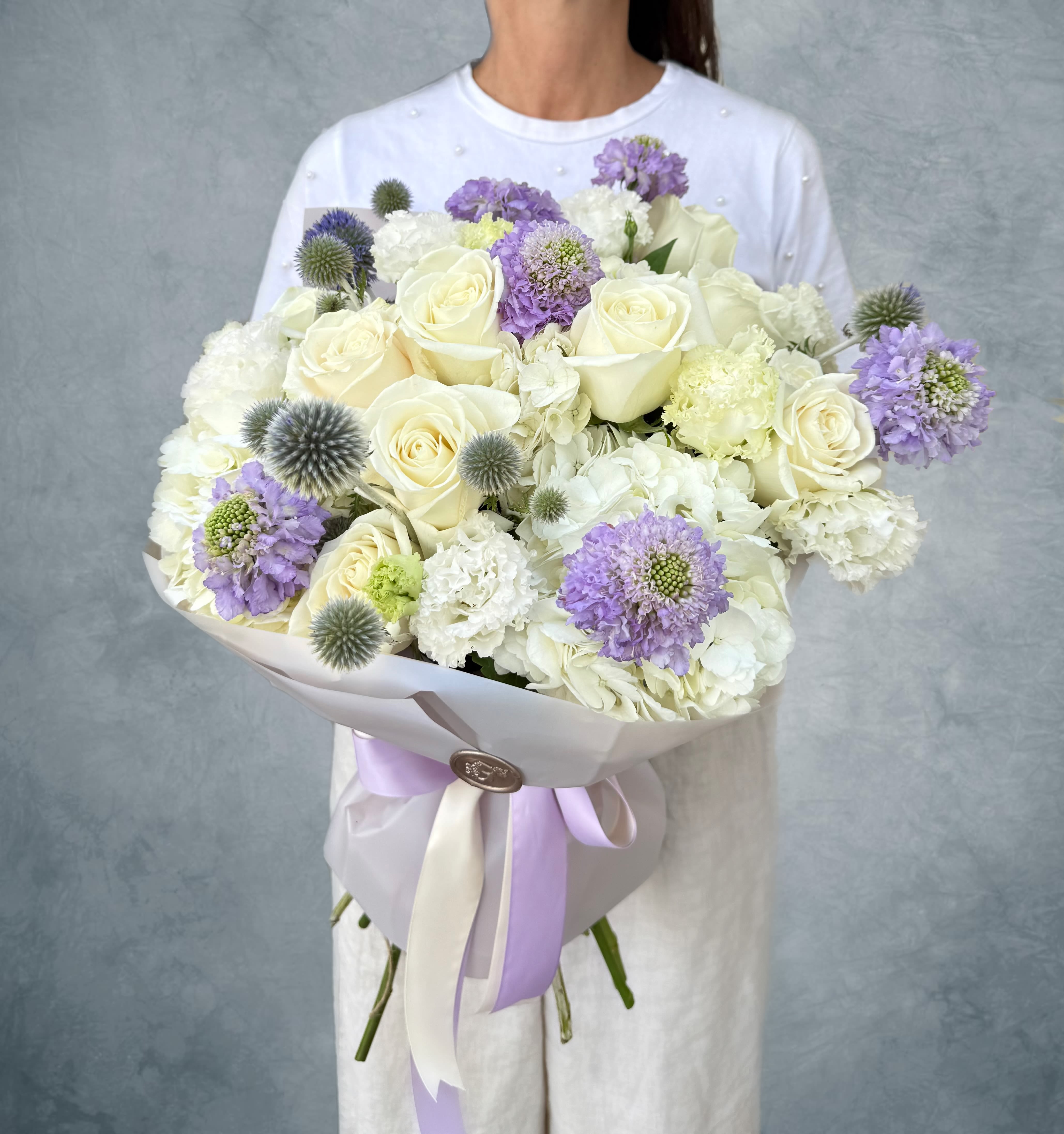 Large bouquet of white roses and lavender flowers wrapped in pale paper